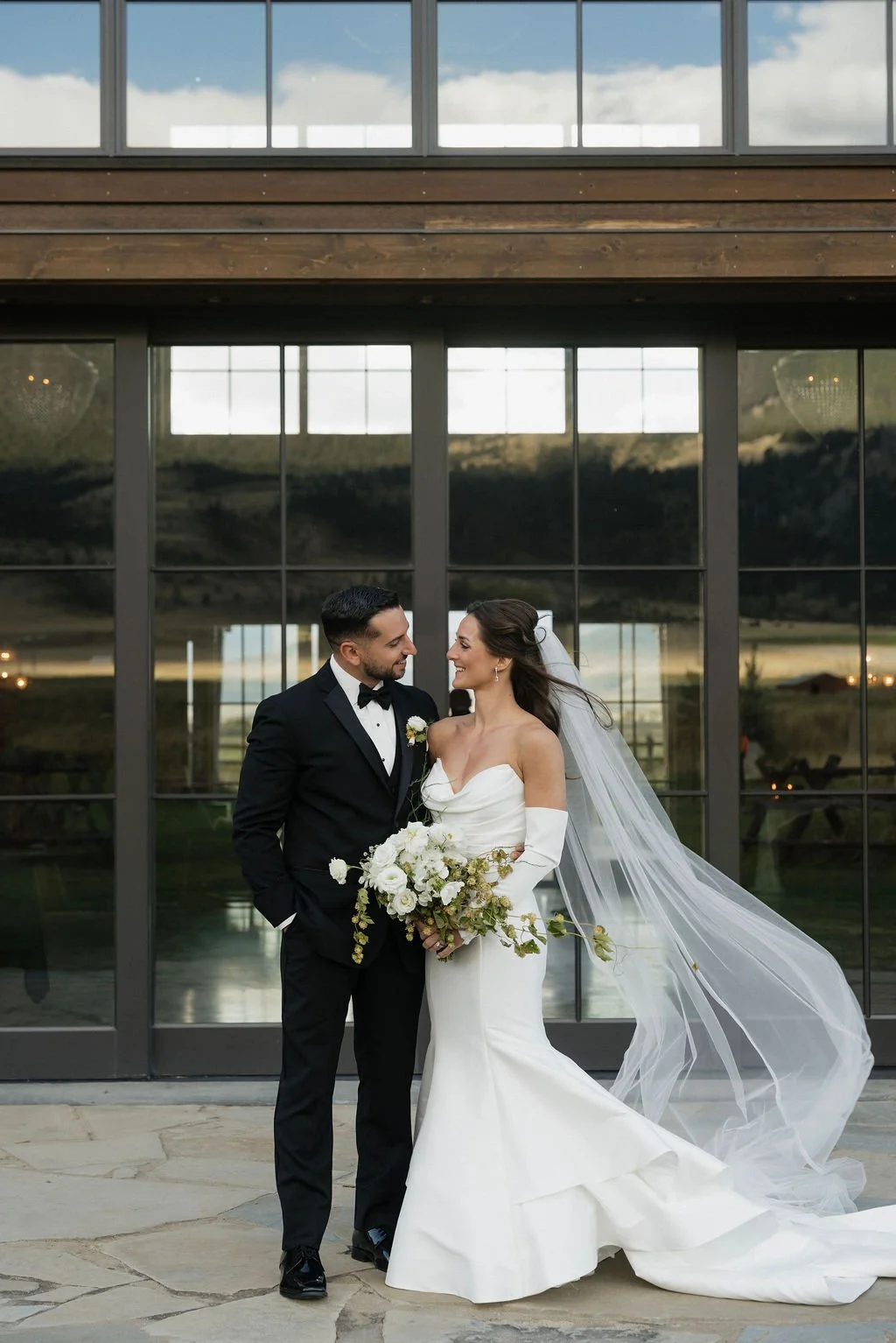 a similar shot of the bride and groom looking at each other outside of the barn at copper rose ranch with the bride's veil blowing in the wind but closer to them