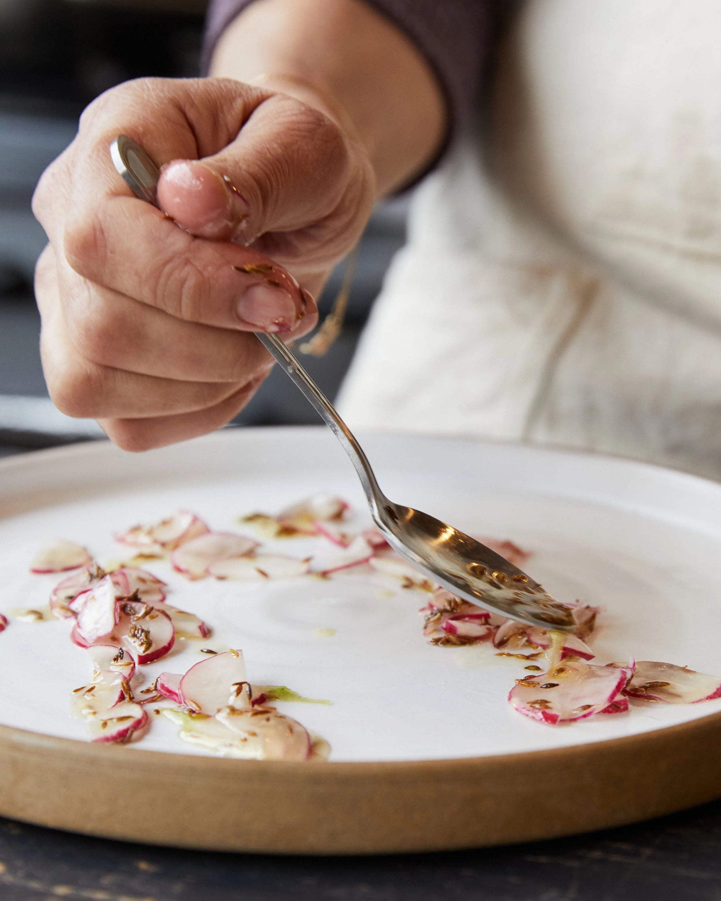 chef plating sliced radishes with cumin oil