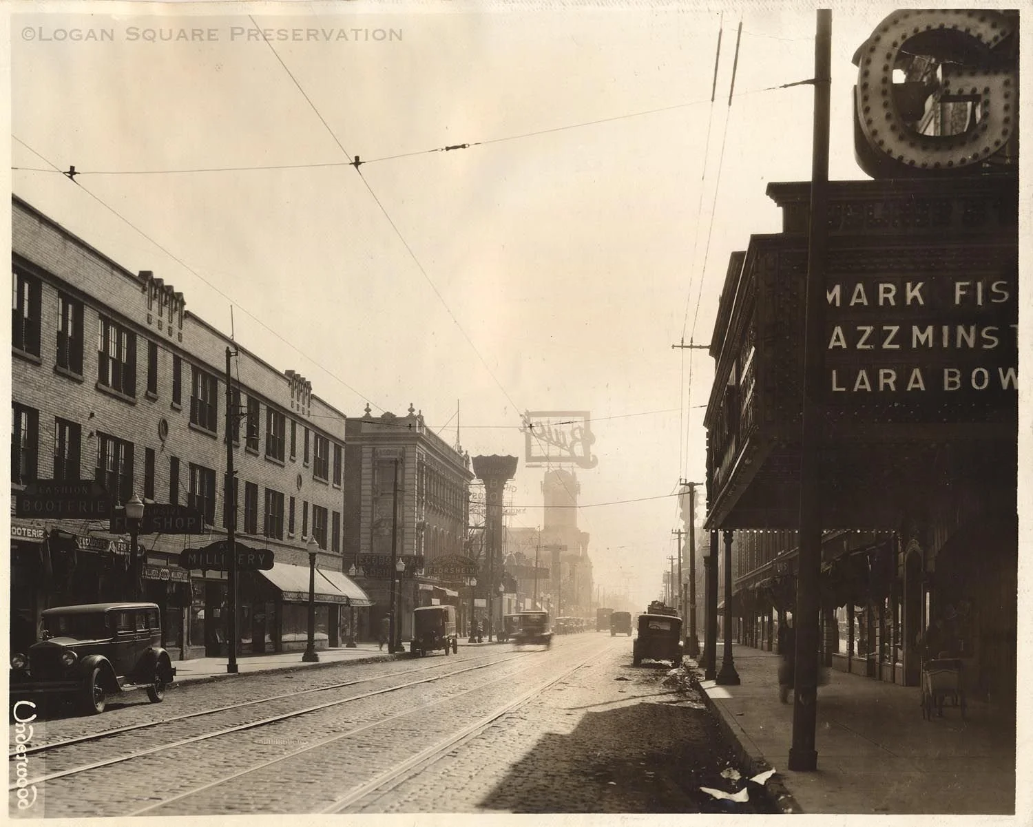 Historical black-and-white street scene showing buildings, parked cars, streetcars, and signs for shops and theaters, with a marquee listing performers.