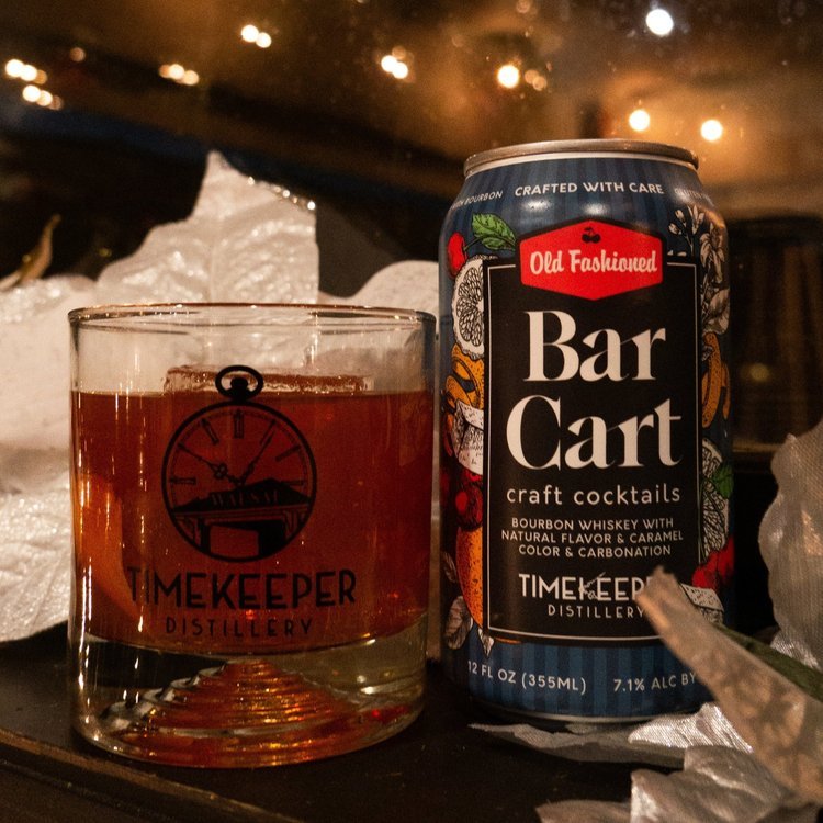 A glass full and can of Timekeeper's Bar Cart Old Fashioned cocktail sit on a bar-top. 