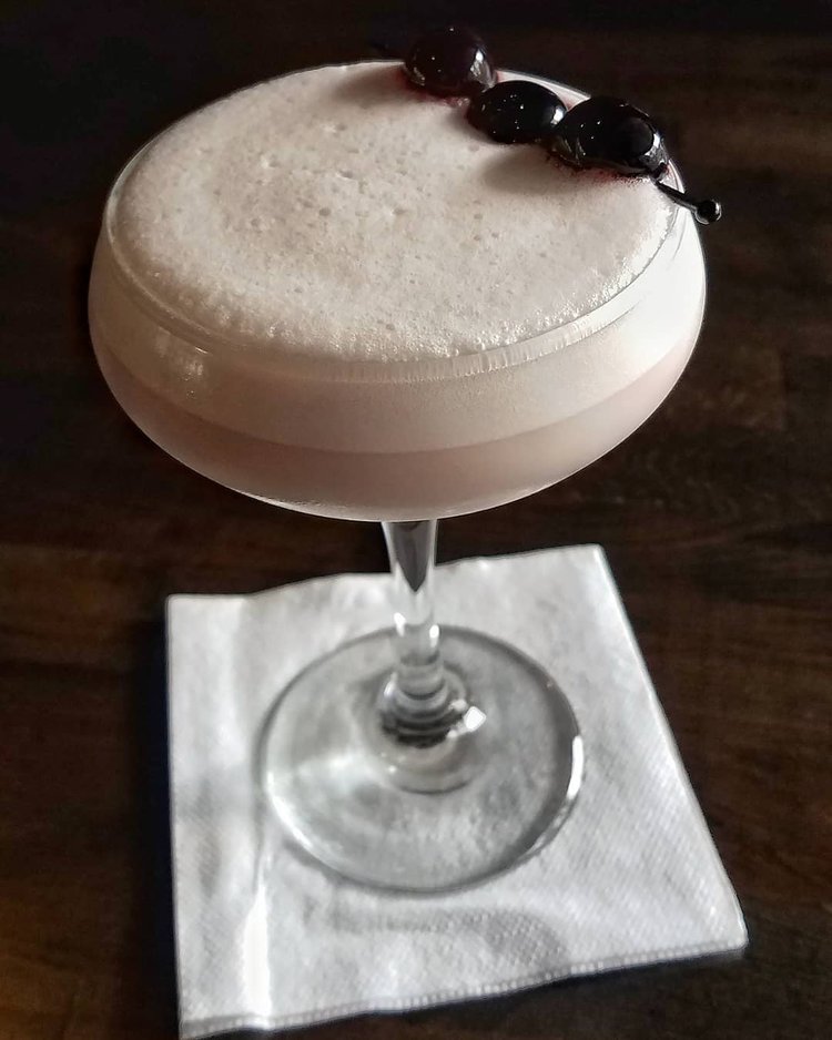A craft cocktail garnished with cherries sit on the bar top at Timekeeper Distillery.