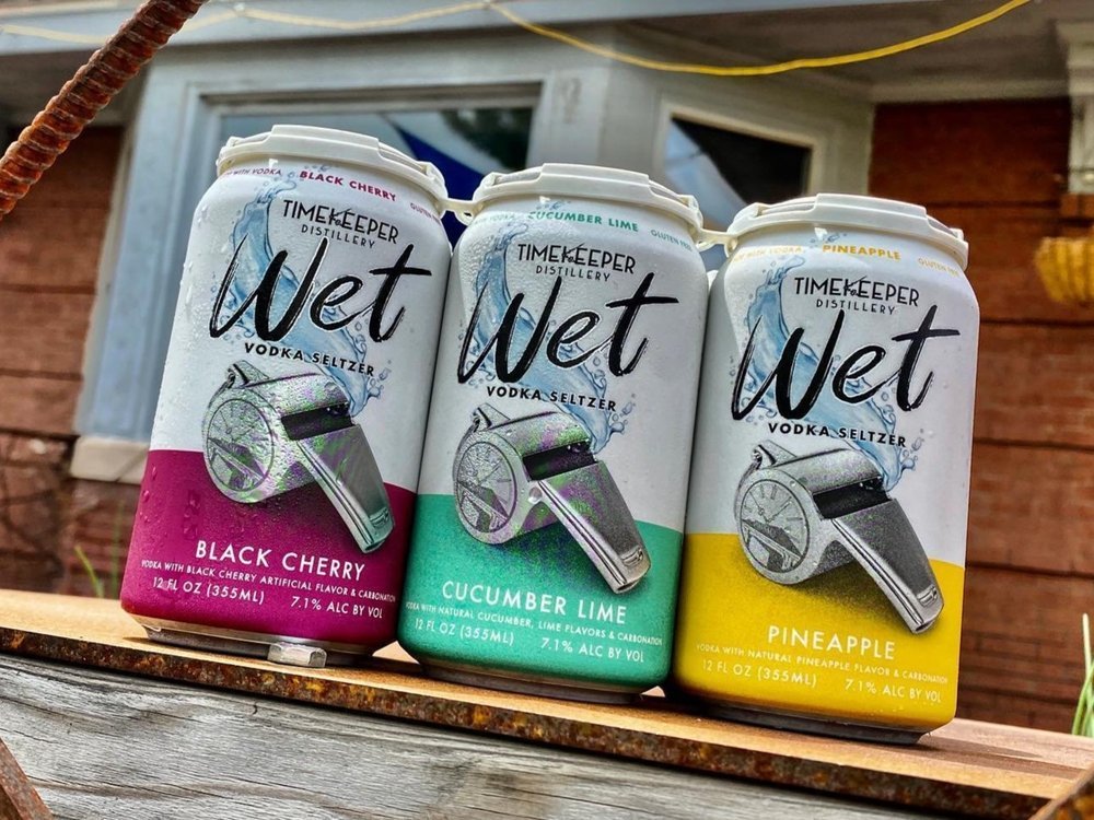 Three flavors of canned WET Seltzers sit on an outdoor patio table at Timekeeper Distillery. 