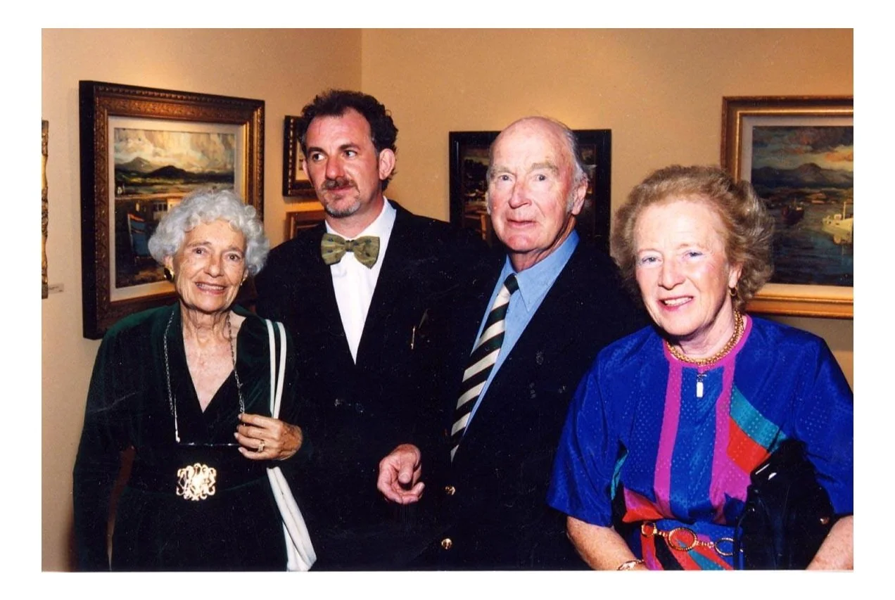 Four people, two women and two men, posing for a photo in an art gallery with landscape paintings on the wall.