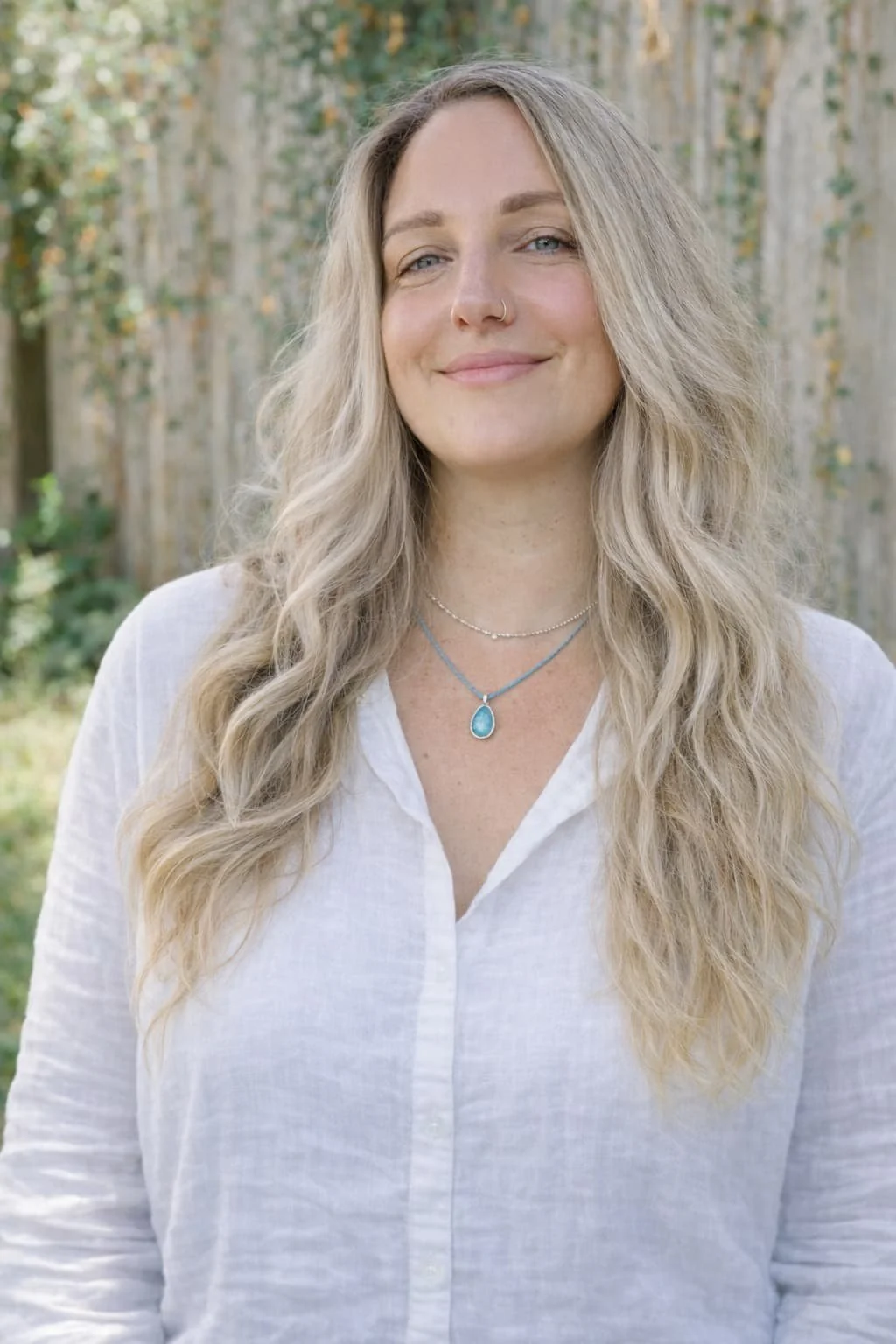 Dr. Sophia Santamaria with long, wavy blonde hair smiling outdoors, wearing a white shirt and layered necklaces, with a background of trees.