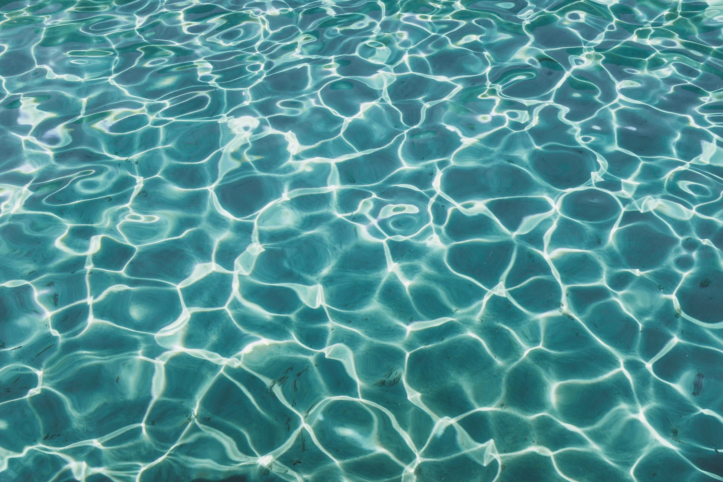 A close-up view of swimming pool water with sunlight reflecting off the surface, creating a pattern of ripples and light.