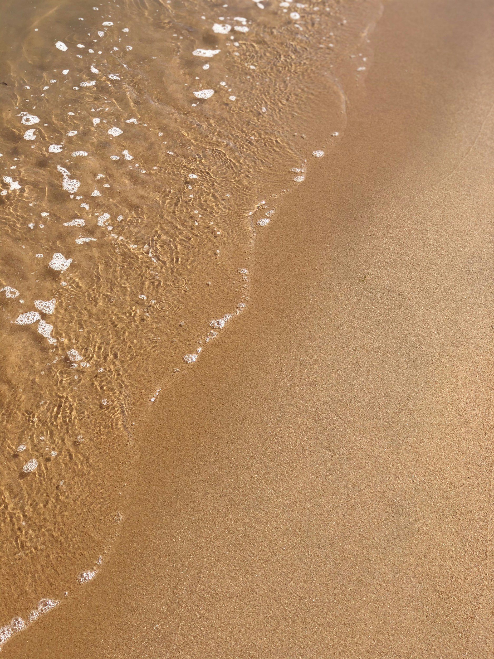 A sandy beach with gentle waves and foam washing ashore.