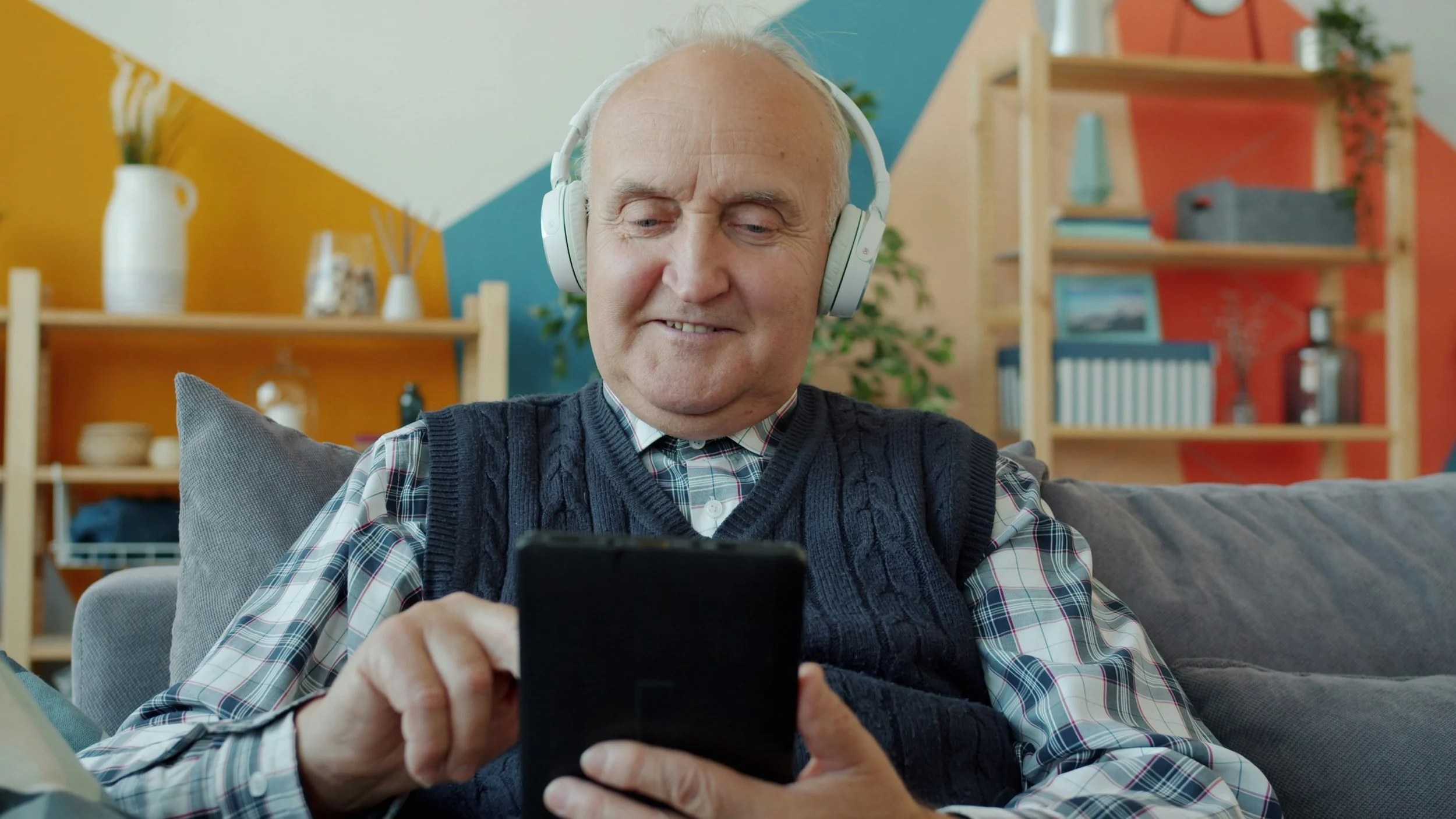 An elderly man enthusiastically using a digital device while wearing headphones.