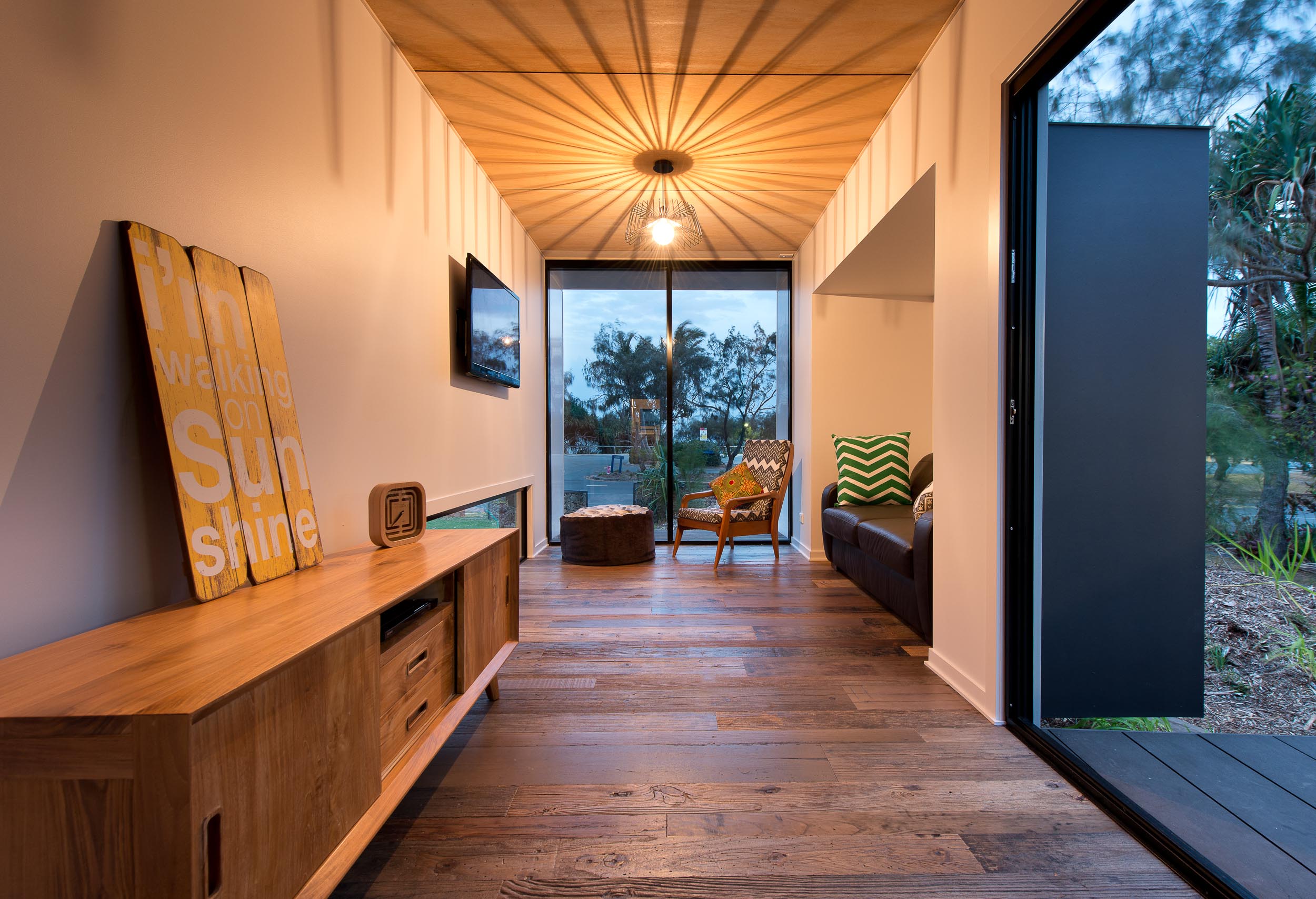 The primary objective was to deliver a modern house with a very simple method of construction and very modest budget with an architectural language that could be regarded as being both gritty and refined, and both urban and coastal. Features such as full height glazing to the ends of the modules, hardwood timber cladding fins, plywood lined roof over the deck and the sleek white alpolic awnings, create a striking architectural composition. The plan arrangement of the 3 modules at splayed angles and separated from each other with linking decks and an internal sitting area, create a dynamic and playful series of spaces.
