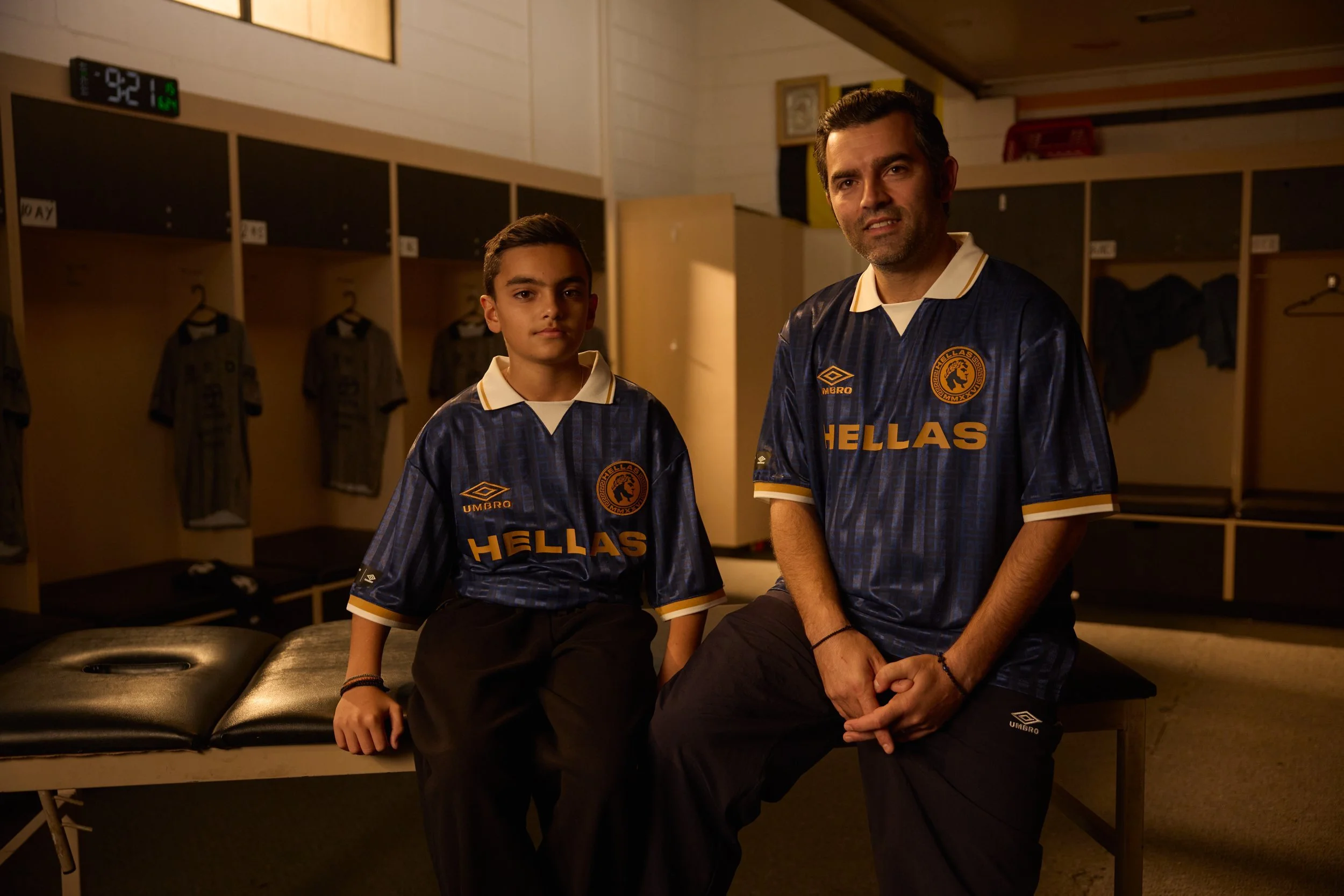 Two generations wearing Umbro Hellas jerseys in a football club changing room