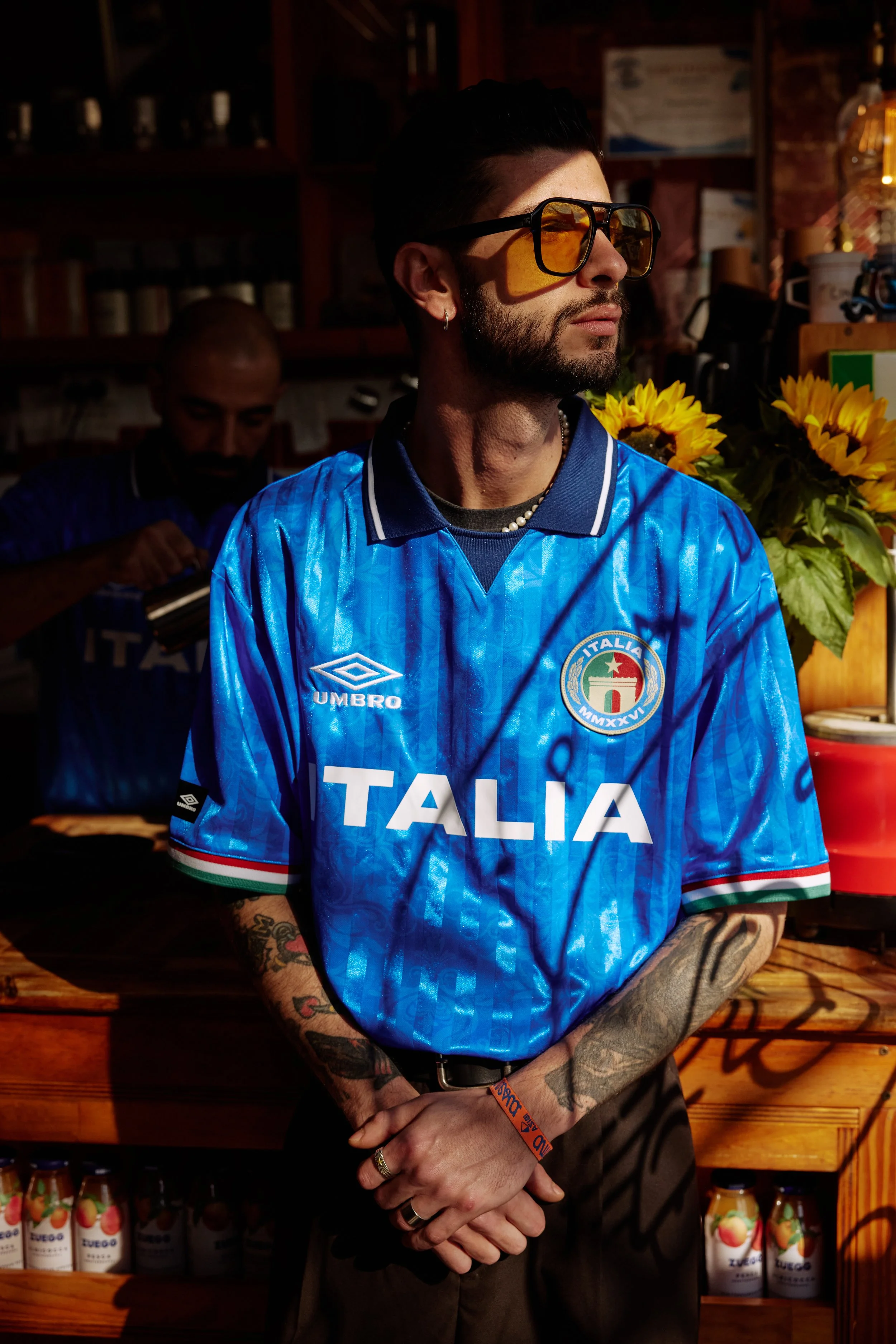 Man wearing a blue Umbro Italia football shirt and sunglasses in a sunlit cafe