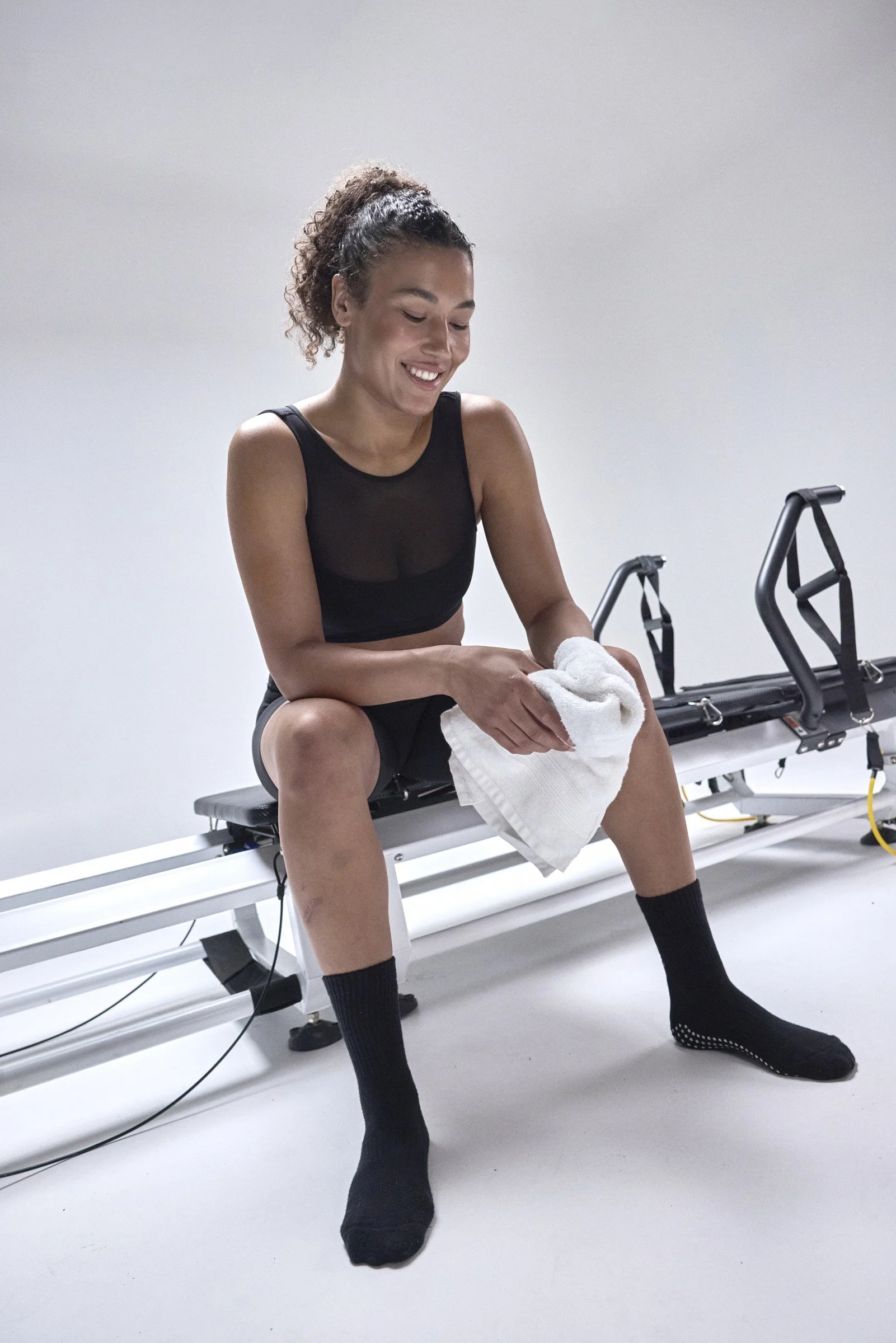 STRONG Pilates athlete seated on a reformer with a towel