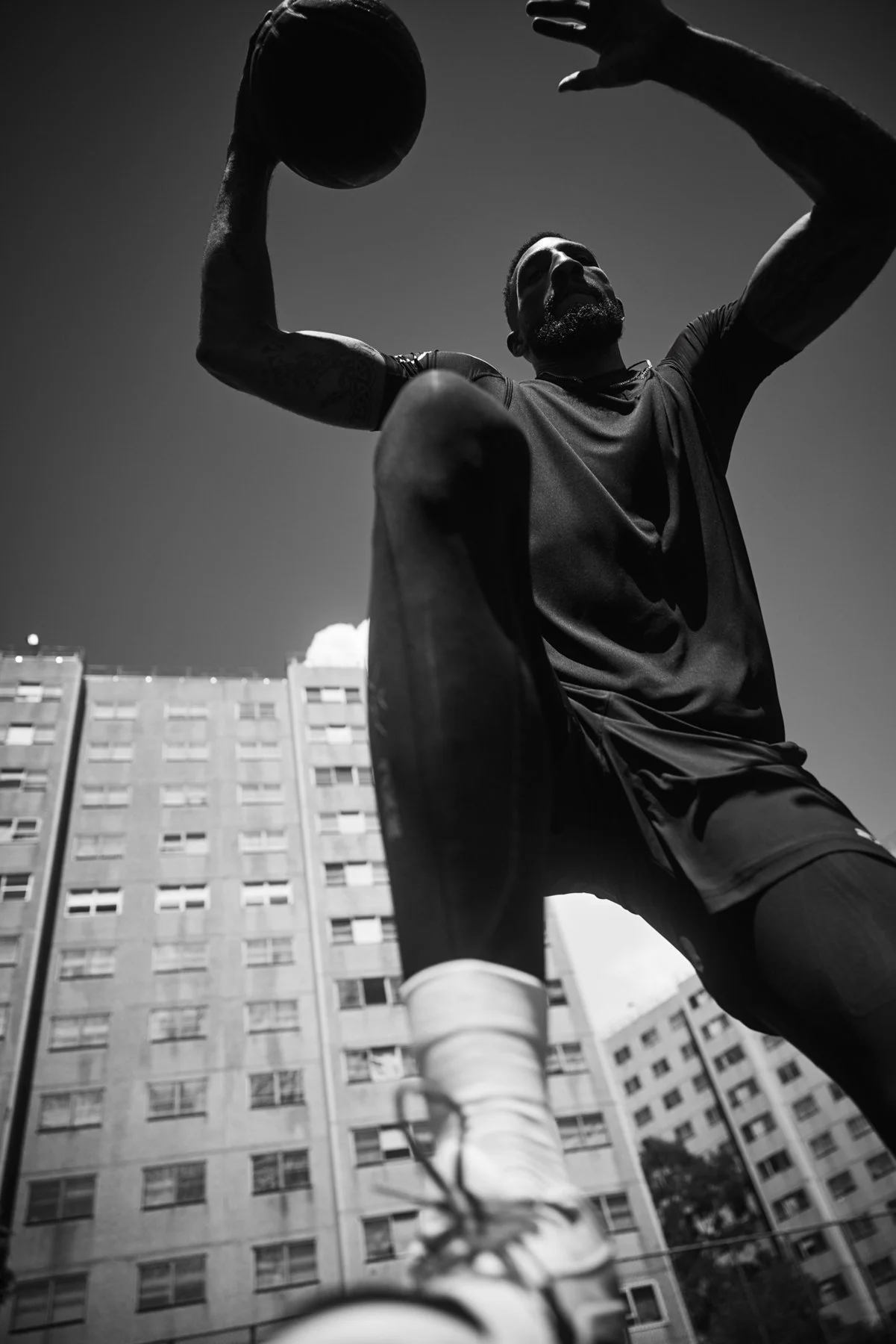 Black-and-white low-angle portrait of Marcus Lee on an outdoor basketball court in 2XU sportswear