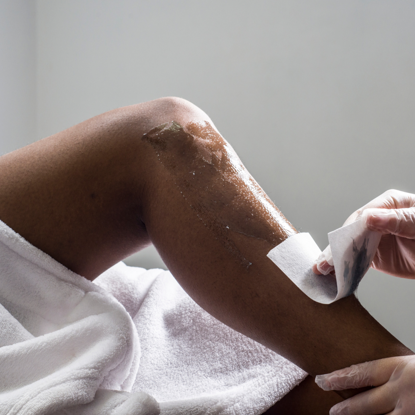 Person receiving a waxing treatment on their upper arm, with wax being applied and a cloth being used to remove excess wax.