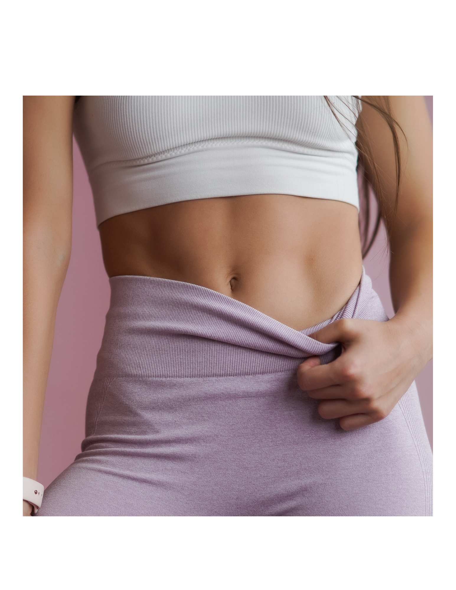 Close-up of a woman with toned abs, wearing a white crop top and pinkish-purple athletic pants, lifting the waistband slightly with her right hand.