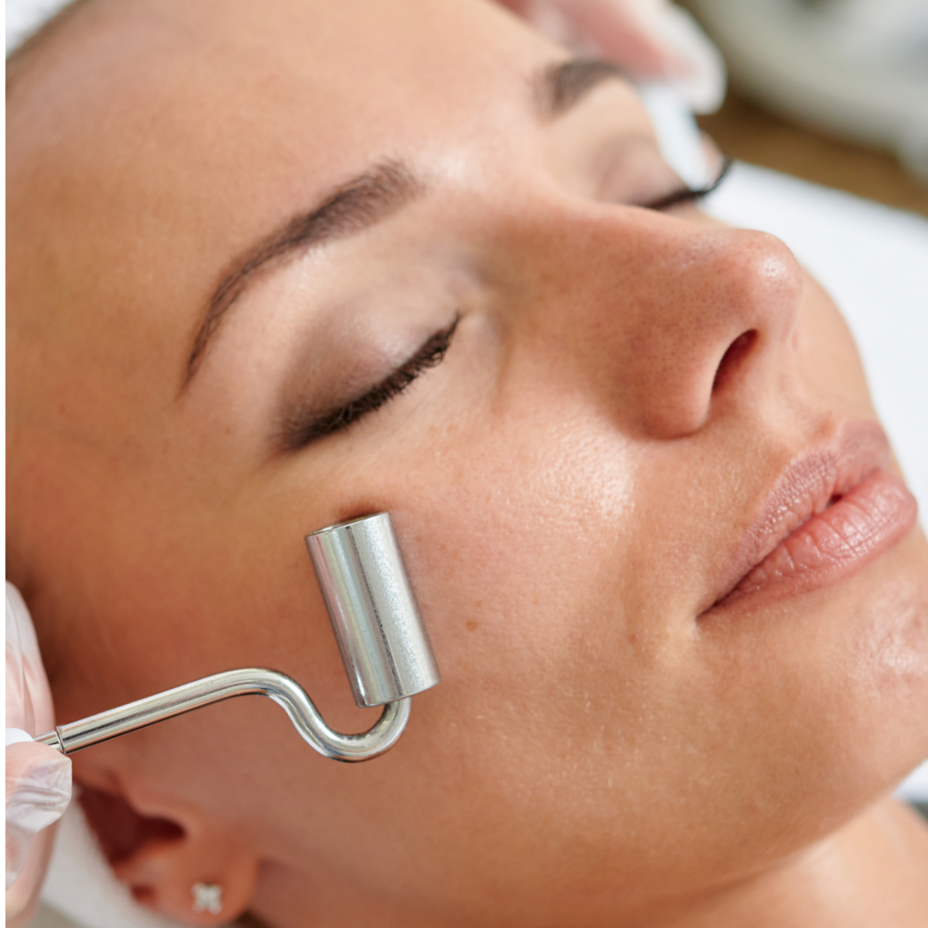 Close-up of a woman receiving a facial treatment, with a skincare roller being used on her cheek.
