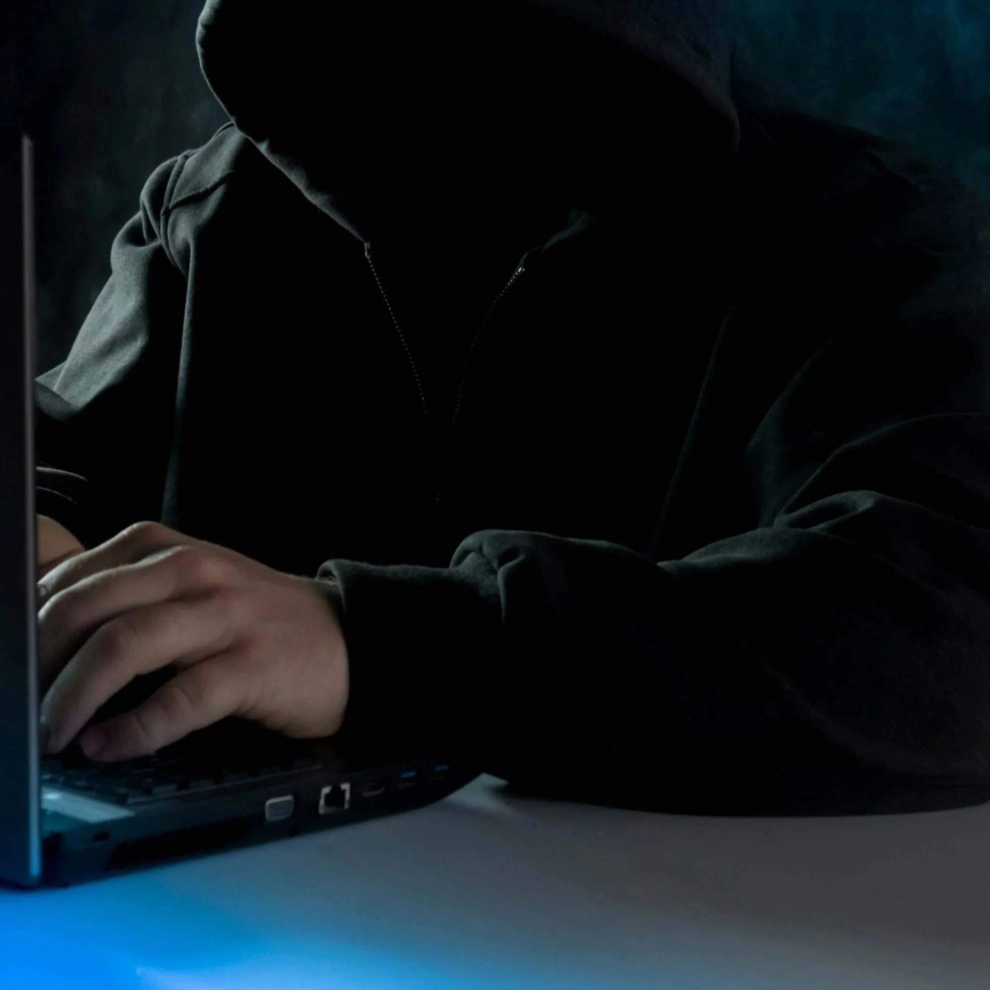 Stock photo of arm clad in black with hand hovering over a laptop.