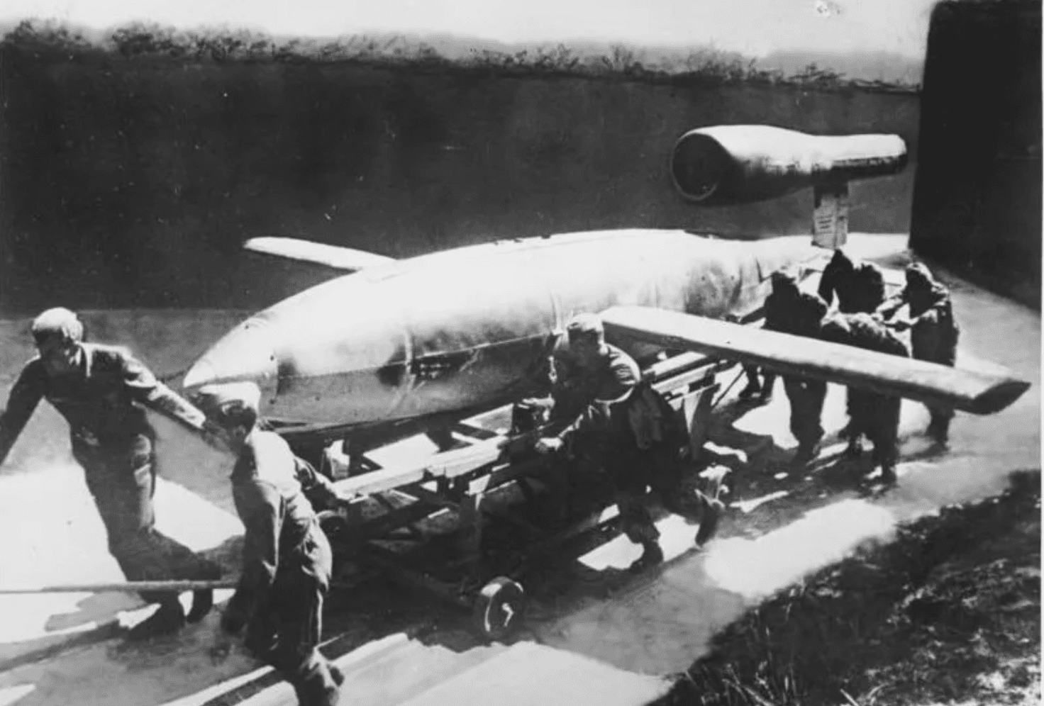 Old black and white photo fo soldiers hauling a large bomb on a trolley.
