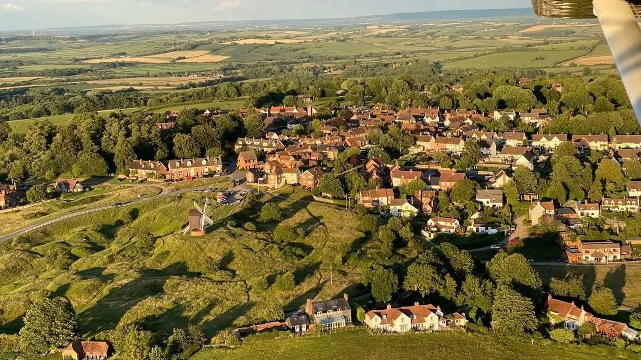 Aerial view of village with lots of trees and fields and distant horizon.