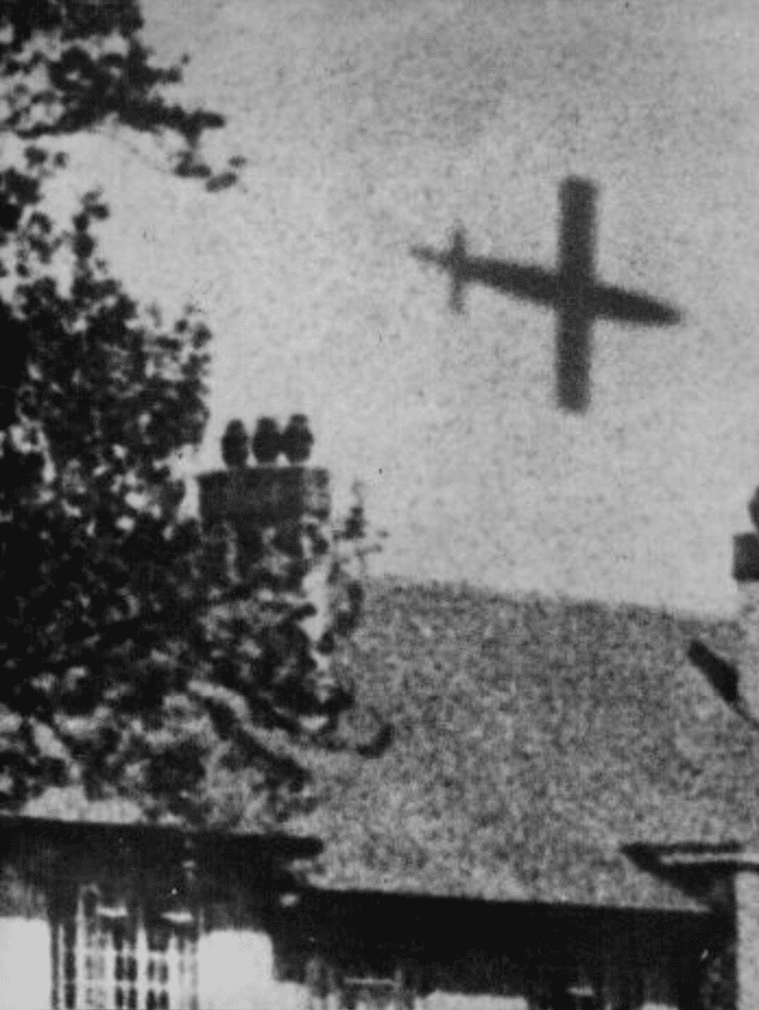 Old black and while photo of a large missile flying over houses.