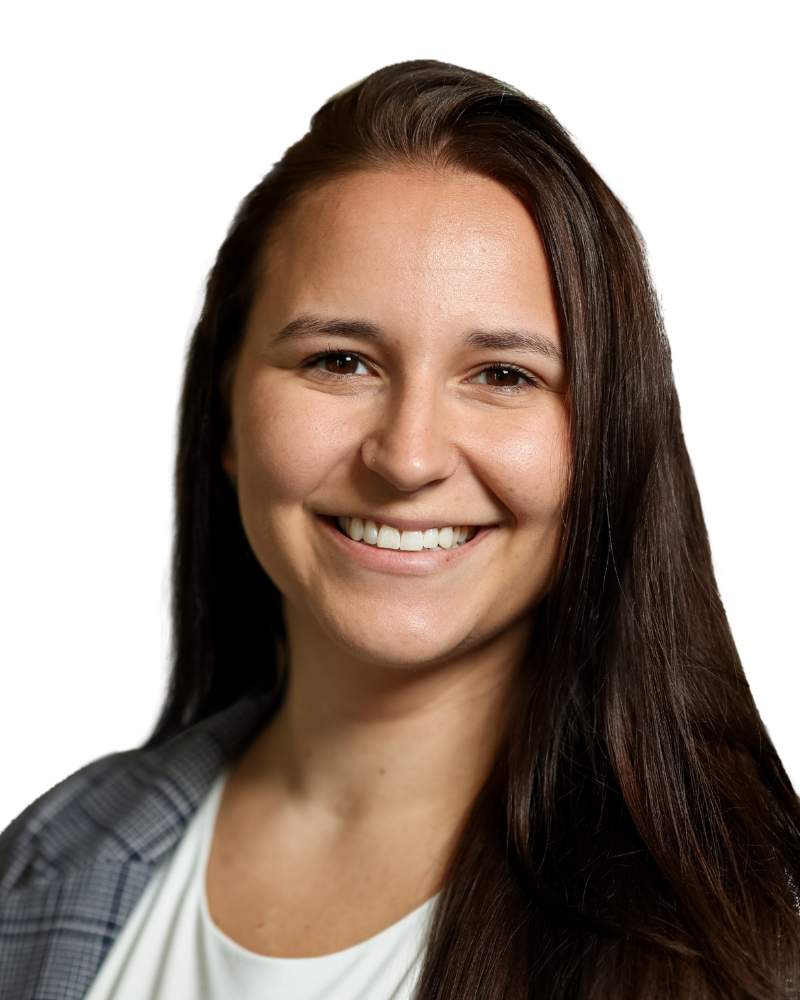 Portrait of a smiling woman with long brown hair, fair skin, wearing a plaid blazer and white top.