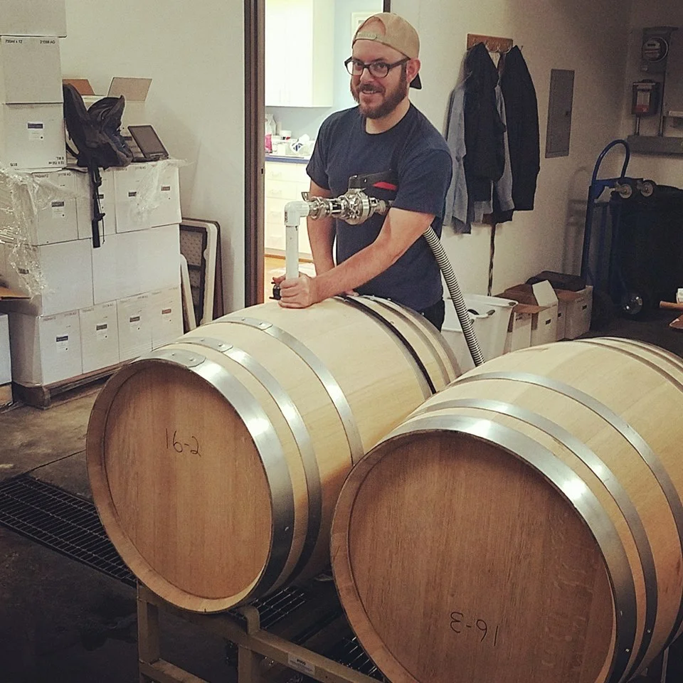 Colin Duddy posing while racking wine from an oak barrel