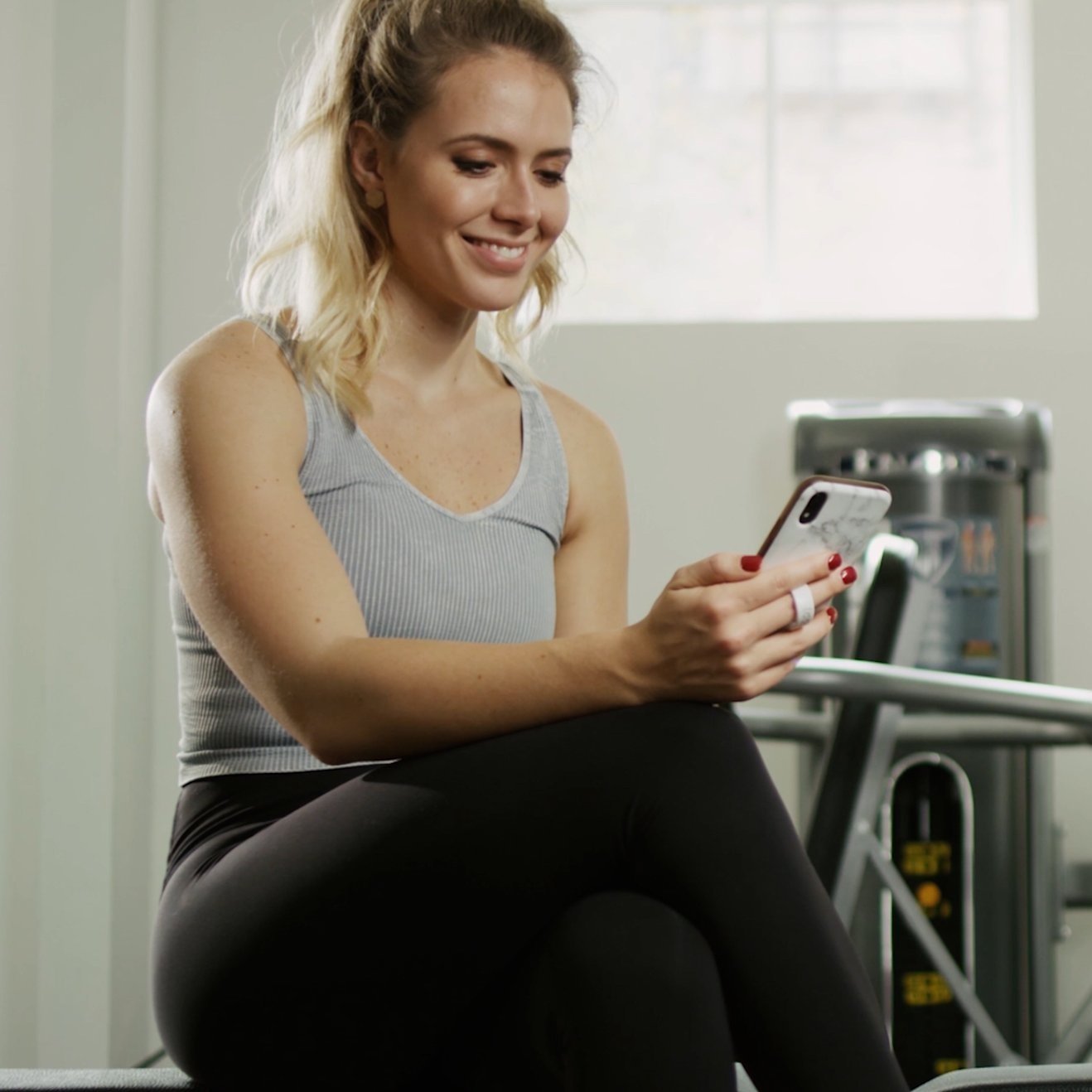 Woman sitting in a gym using her phone during a workout session from an influencer marketing commercial, produced by Killshot Media.