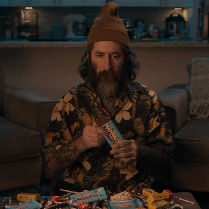 Man sitting on a couch holding a product in a cinematic commercial spot for Mr. Beast "feastables"..