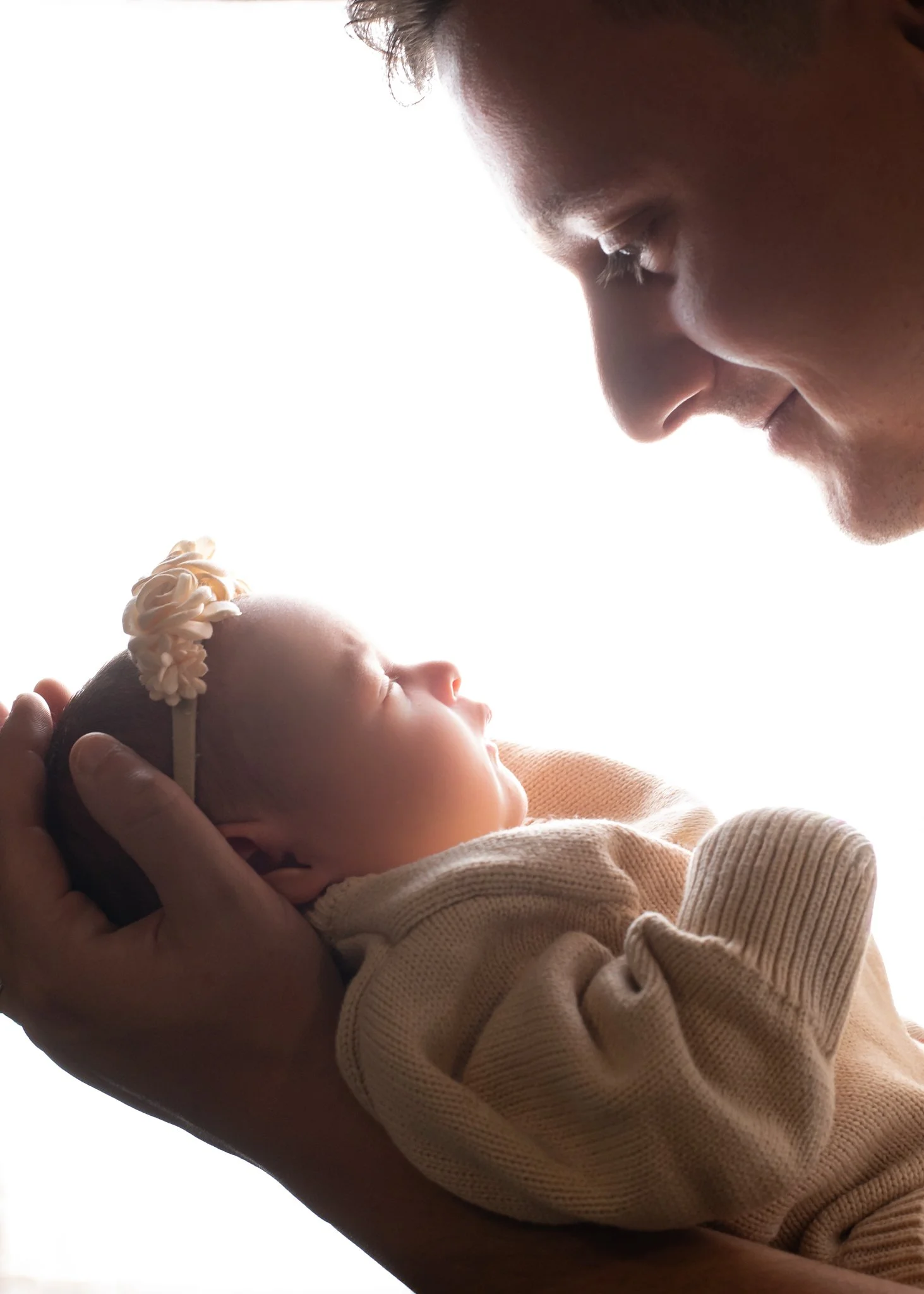 A person holding a sleeping infant close to their face, with both appearing peaceful and calm, against a bright, white background.