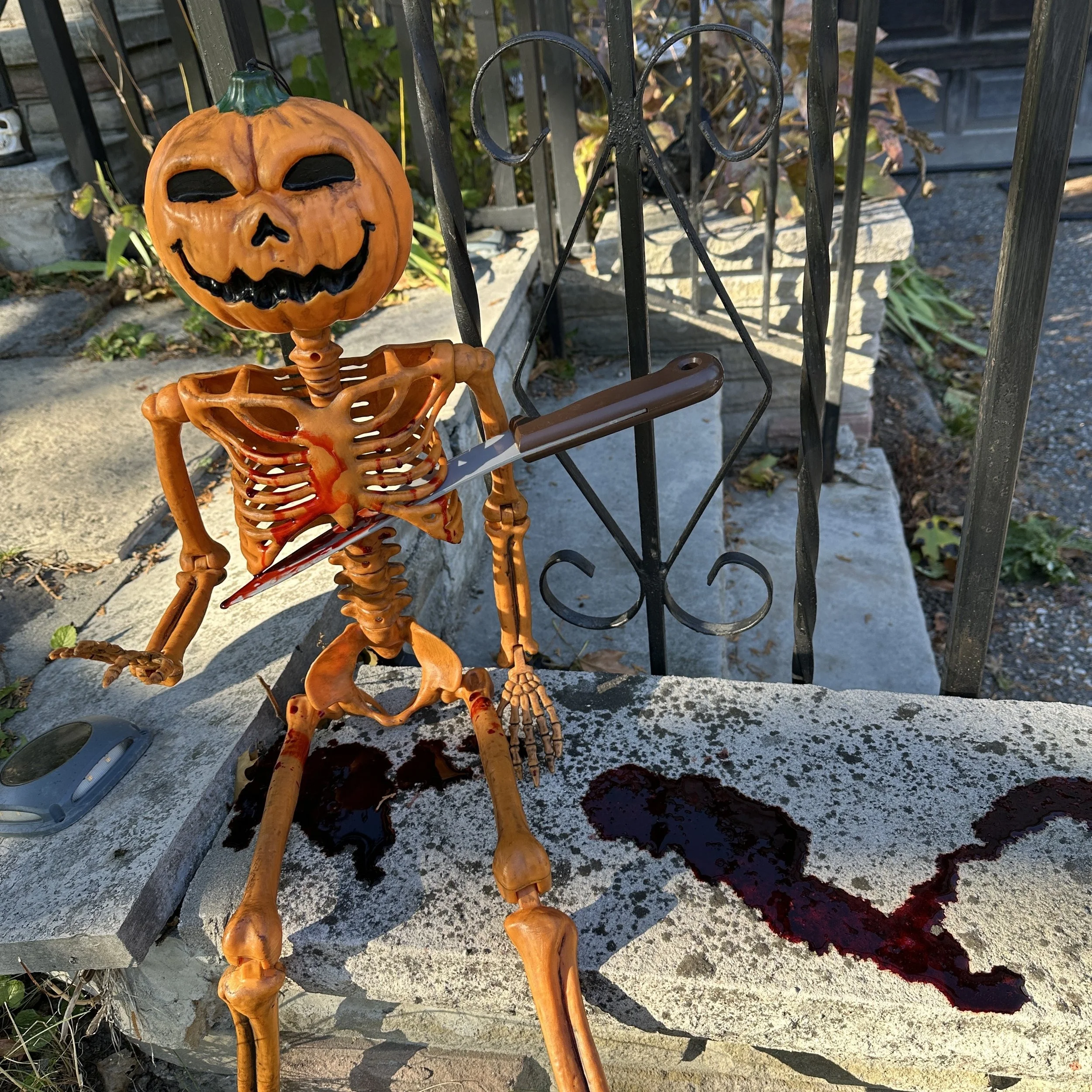 An orange skeleton with a jack-o-lantern for a head. It has a fake knife stuck in its ribs and is dripping with fake blood.