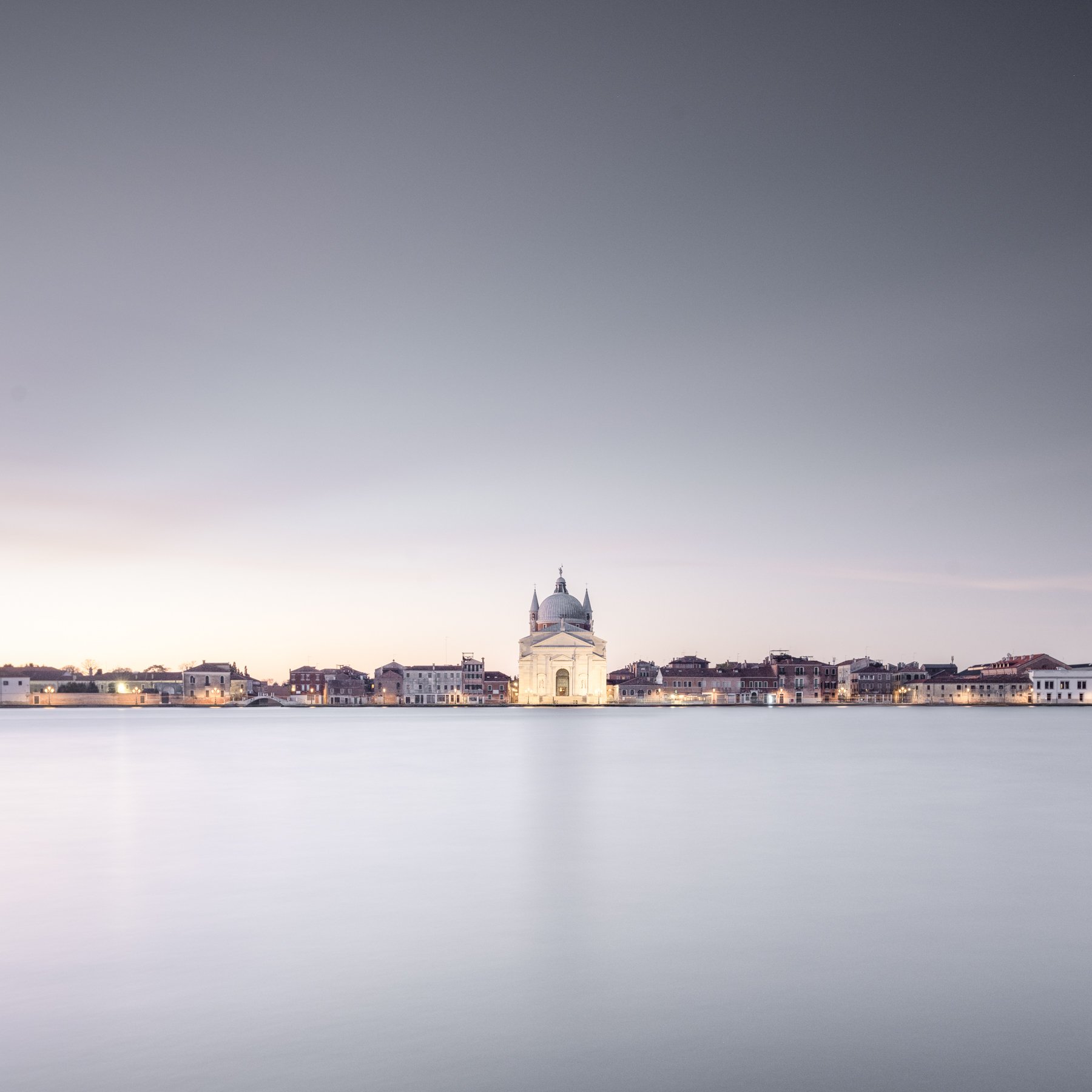 Redentore. Long-exposure photograph of a this Venice church across the lagoon, with a pale sky and soft reflections.