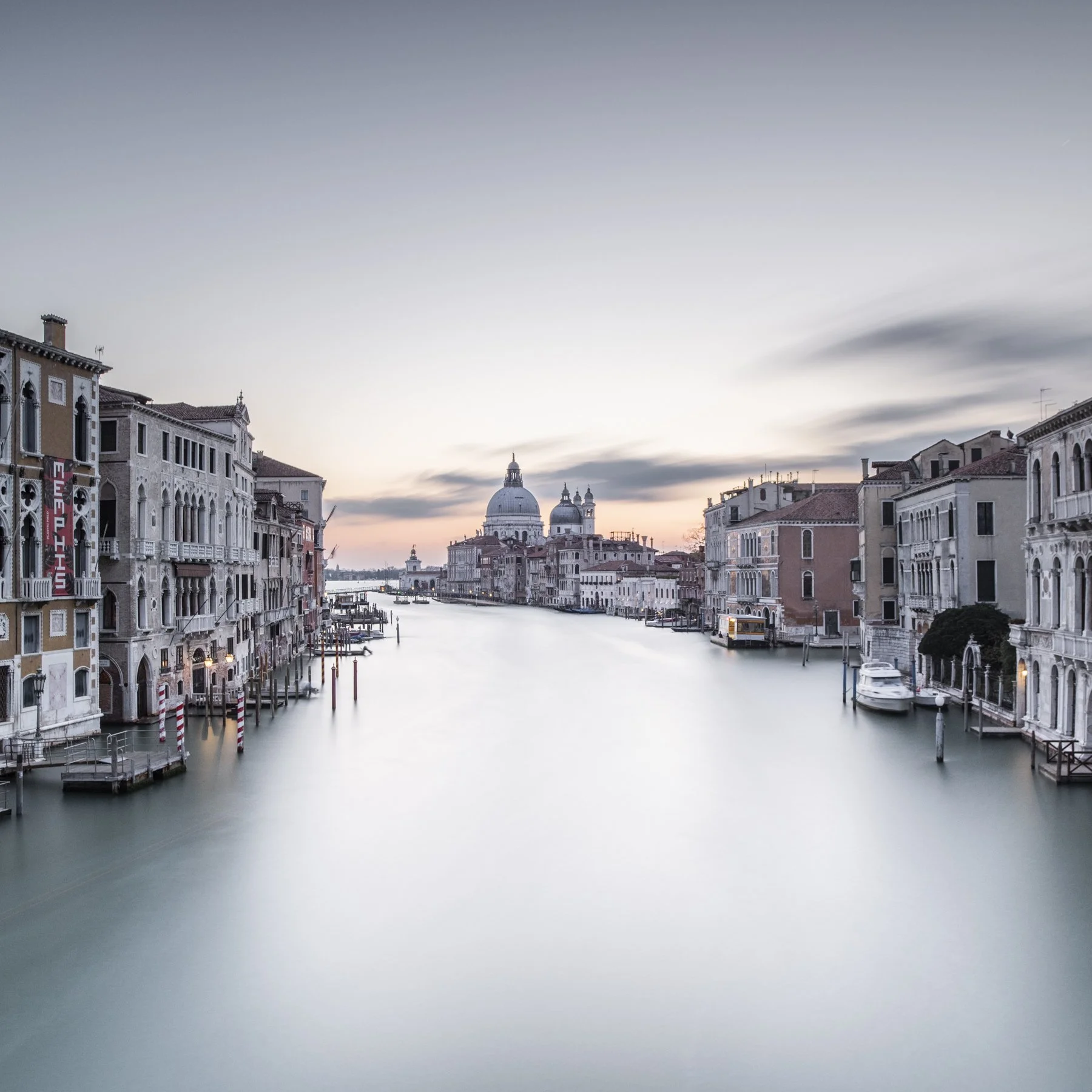 Venetian Dawn. Long-exposure photograph of Santa Maria from Accademia in Venice on the Grand Canal with historic buildings on either side, softened by smooth water and diffused light.