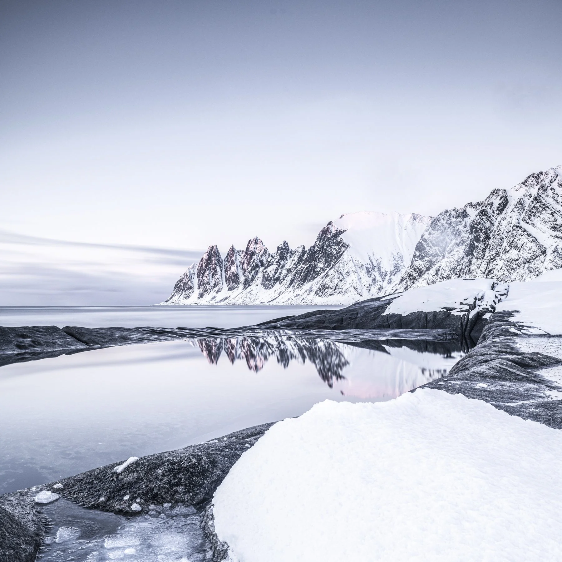 Dragons Teeth. Reflection of mountains in rock pool at coast in Senja in winter. 