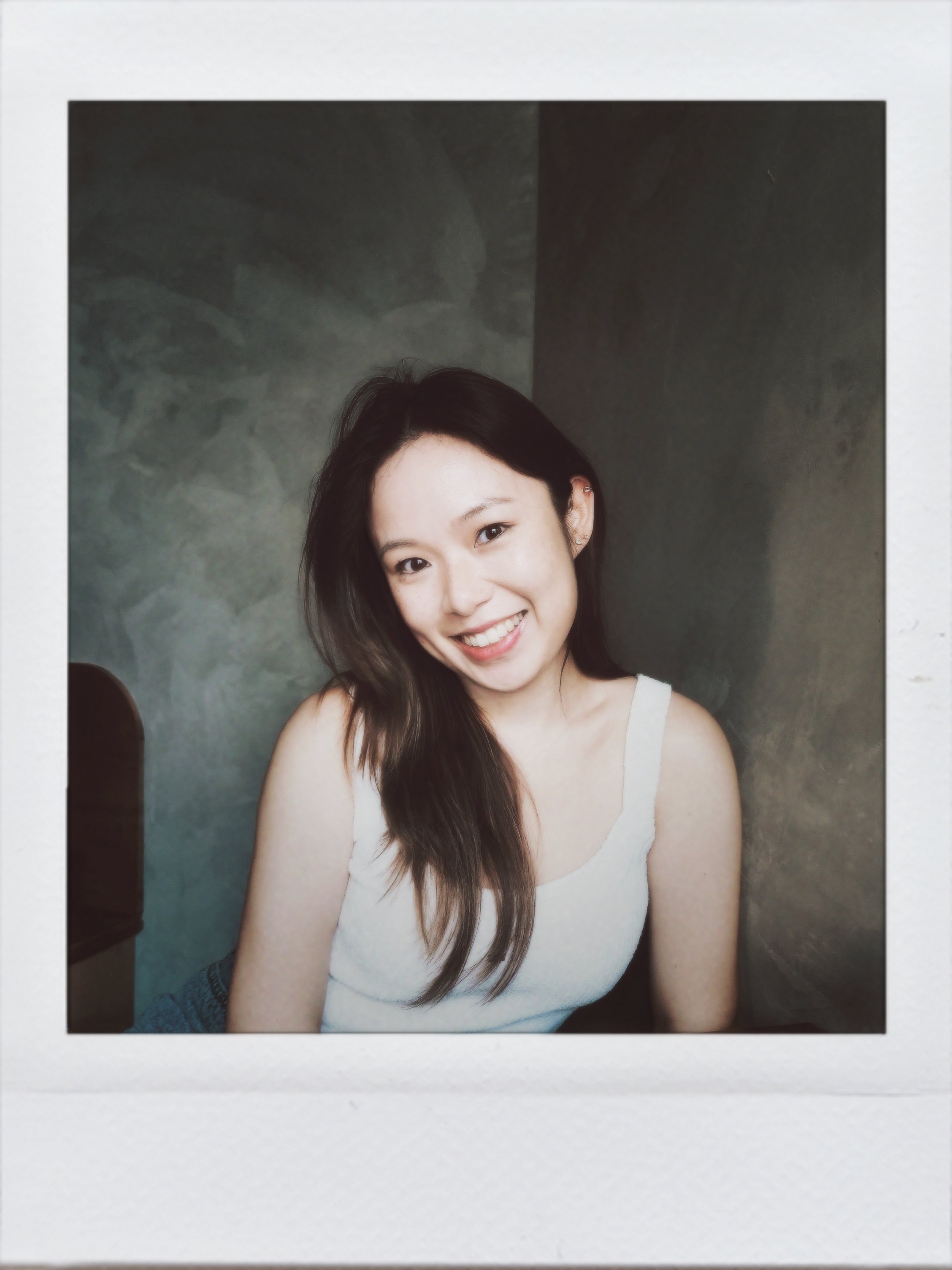 Young woman with long dark hair smiling and sitting against a two-tone background.
