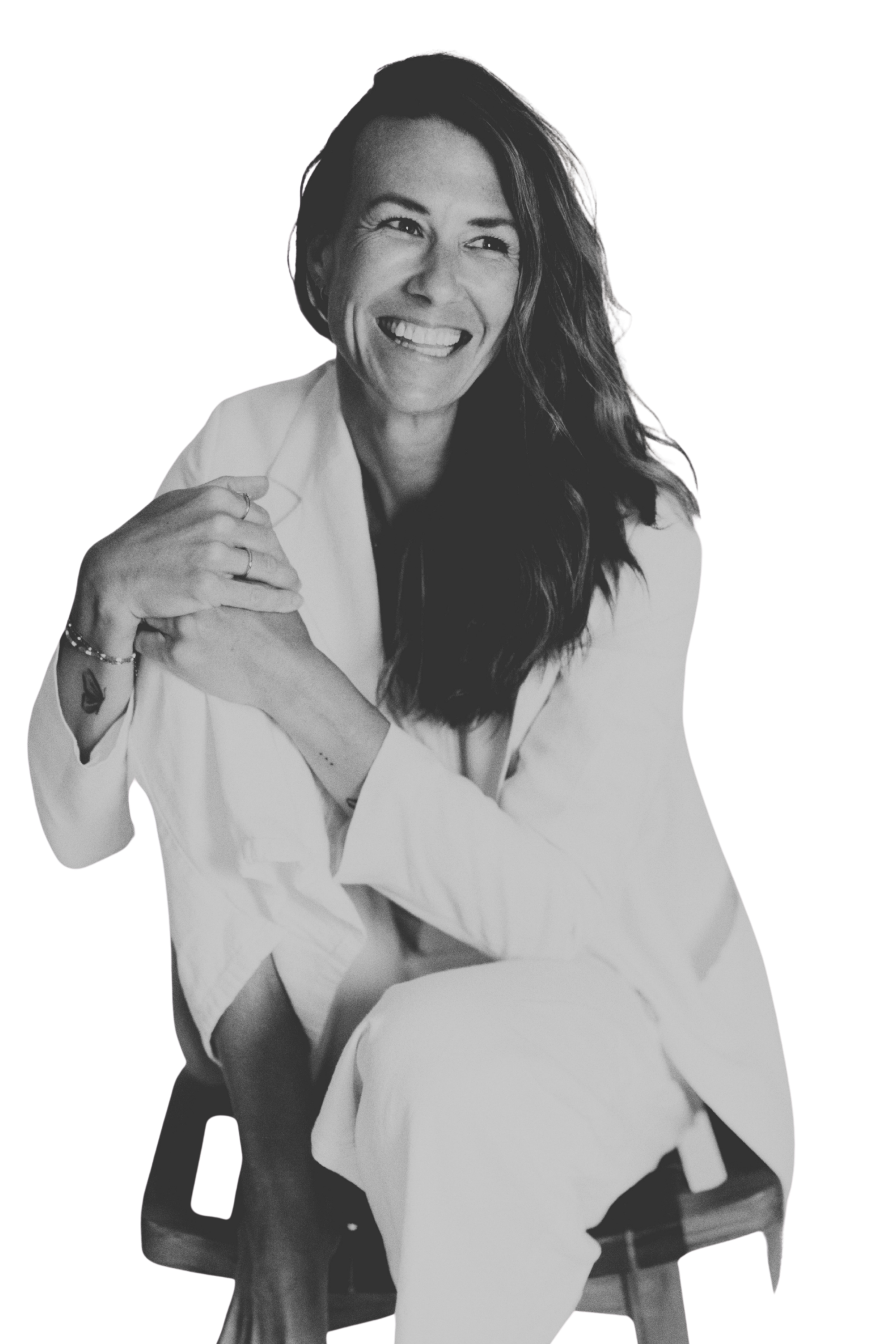 Black and white photo of a woman with long hair smiling, wearing a white shirt, with her arms crossed and hand on her shoulder.
