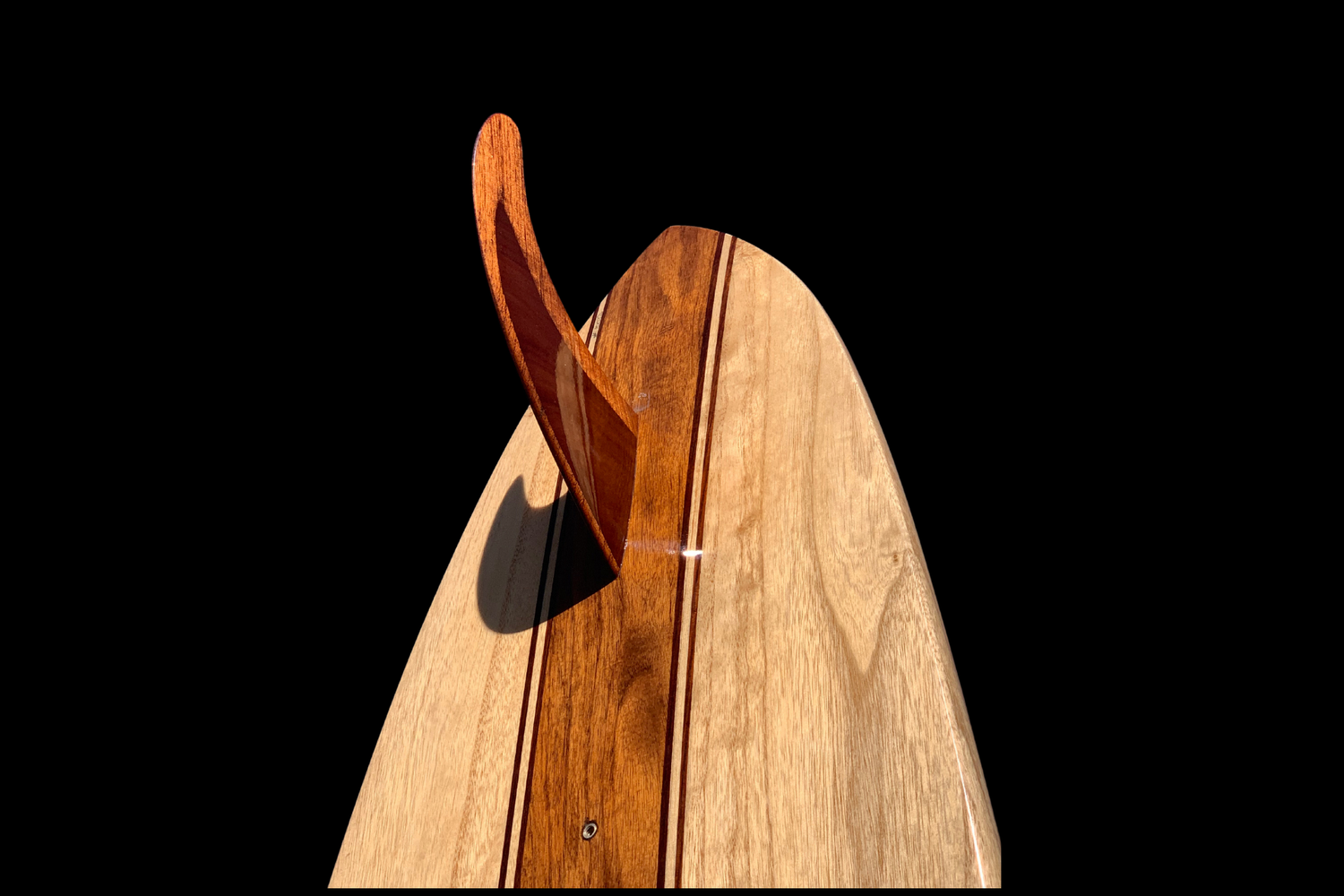 Close-up of a wooden surfboard with a detached fin, photographed on a black background.