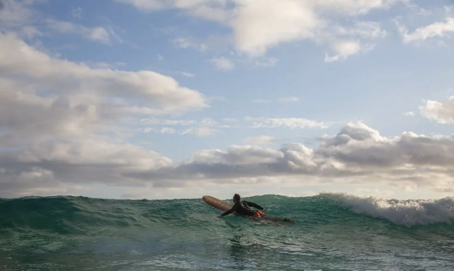 Surfer paddling on a wave in the ocean with partly cloudy sky.