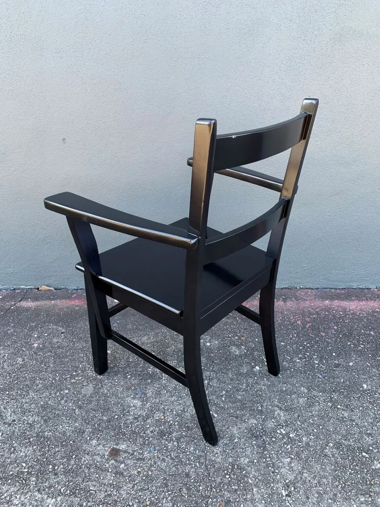 Black wooden chair with armrests and a backrest, placed on a concrete surface against a plain light gray wall.