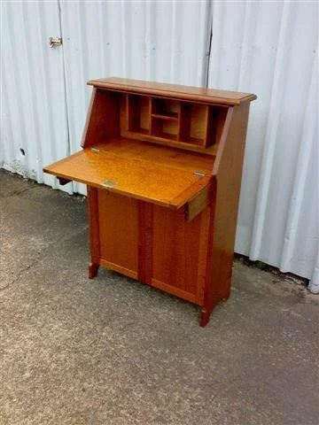 Wooden secretary desk with hutch, placed outdoors on concrete ground against a white corrugated metal wall.