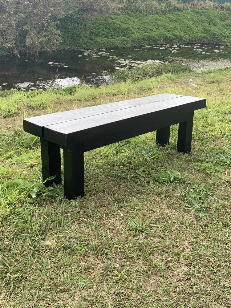 A black wooden bench on a grassy area near a pond with green hills in the background.