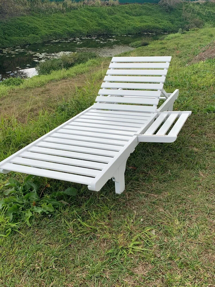 White lounge chair on grassy riverbank with water and lily pads in the background.