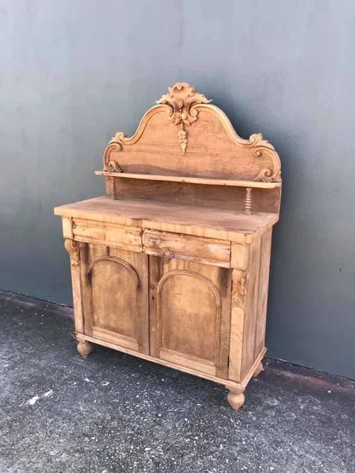 An antique wooden dresser with a decorative back panel and a small shelf, placed against a plain wall.