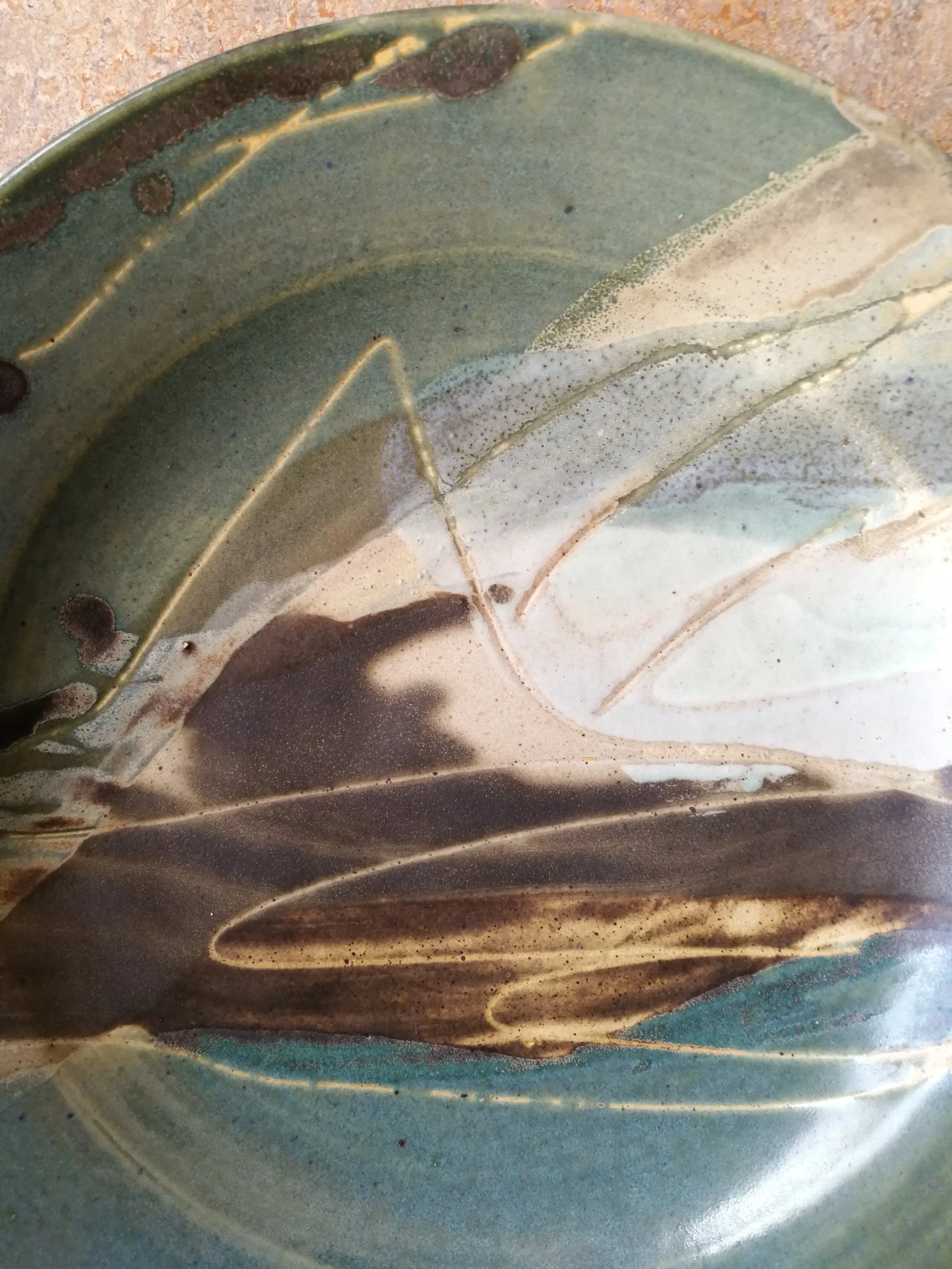Close-up of a ceramic plate with a swirl pattern in shades of green, brown, white, and beige.