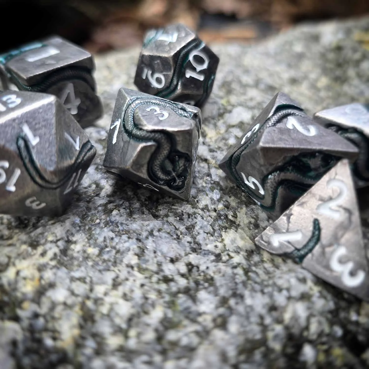 Set de 7 dés polyédriques métalliques pour jeu de rôle, ornés de vipères en relief, avec chiffres clairs et finition vieillie.