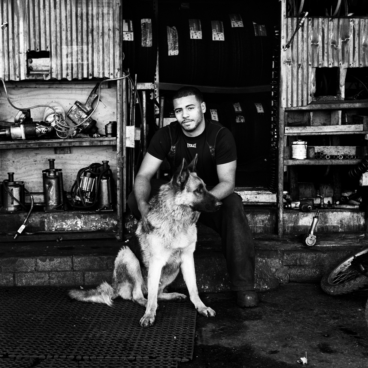  Anthony beside his dog Riley at the entrance to their tire shop, P&amp;J Tire Shop, on Metropolitan Avenue. It was Riley's birthday.  Bushwick, Brooklyn, N.Y. (Nov. 2015) 