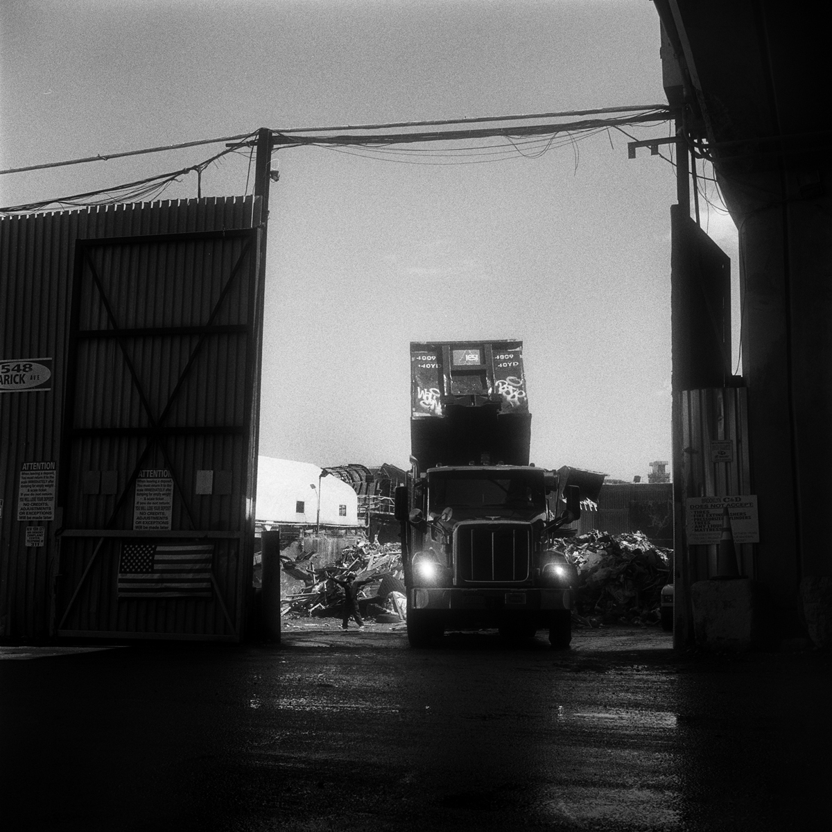  A roll-off truck in the process of dumping its contents as the yard’s spotter hand-signals the driver his container is empty.  Greenpoint, Brooklyn, N.Y. (Sept. 2015) 