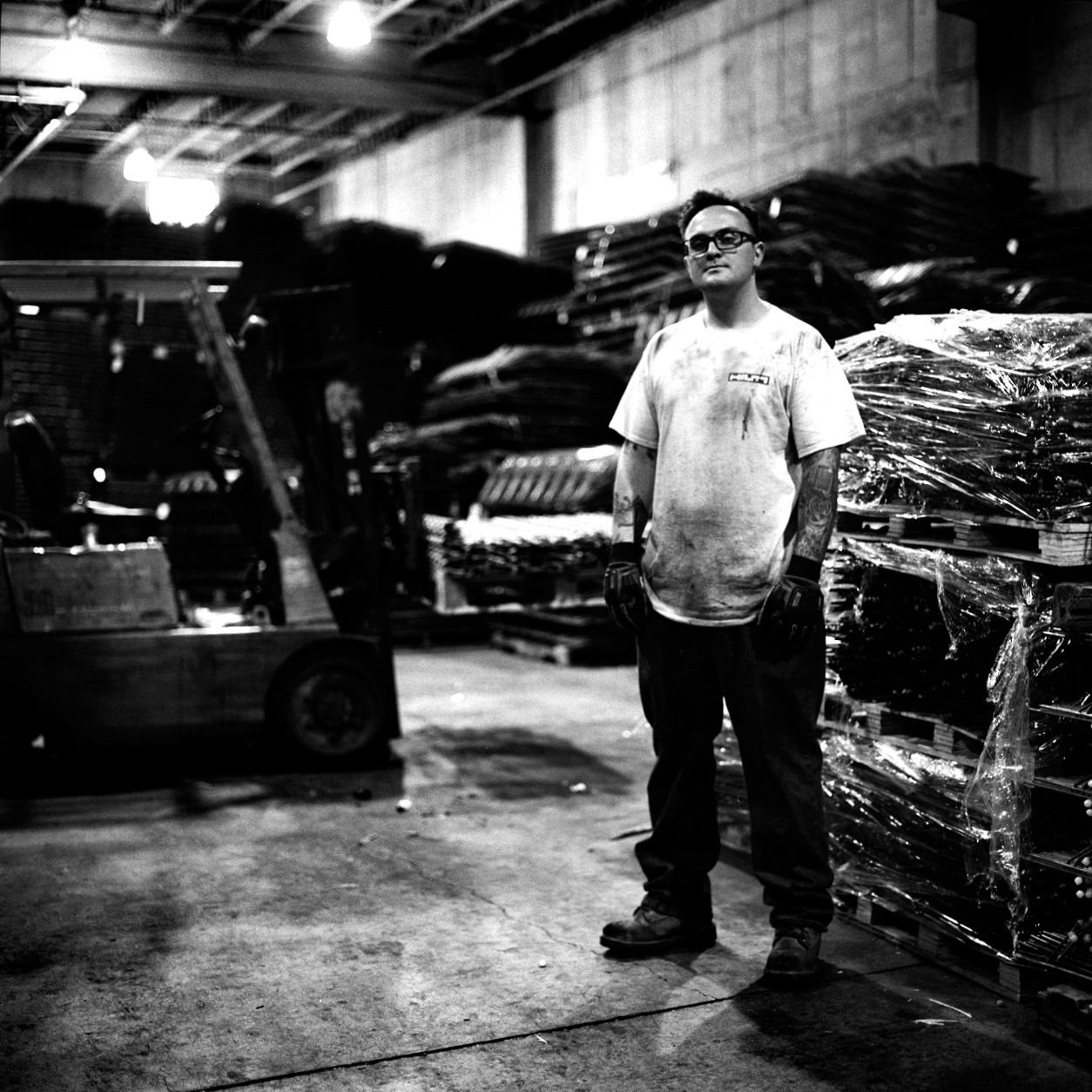  David Goldsmith standing before the sea of chairs he organizes daily with his forklift at Reinforcing Supply. When not on the job he plays with his rock band at a variety of venues.  Williamsburg, Brooklyn, NY (July 2016) 
