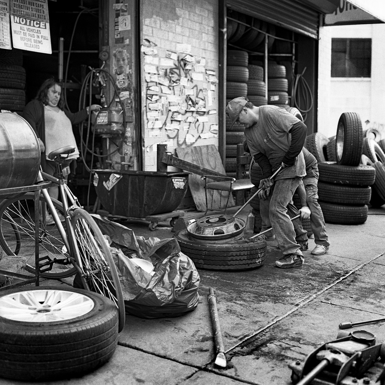  Northside Tire Shop employees from Scott Ave wrestling with a rim and tire. The process, handled by specified machines at other shops, is done by hand here with only the help of some elbow grease.  Bushwick, Brooklyn, N.Y. (Oct. 2015) 