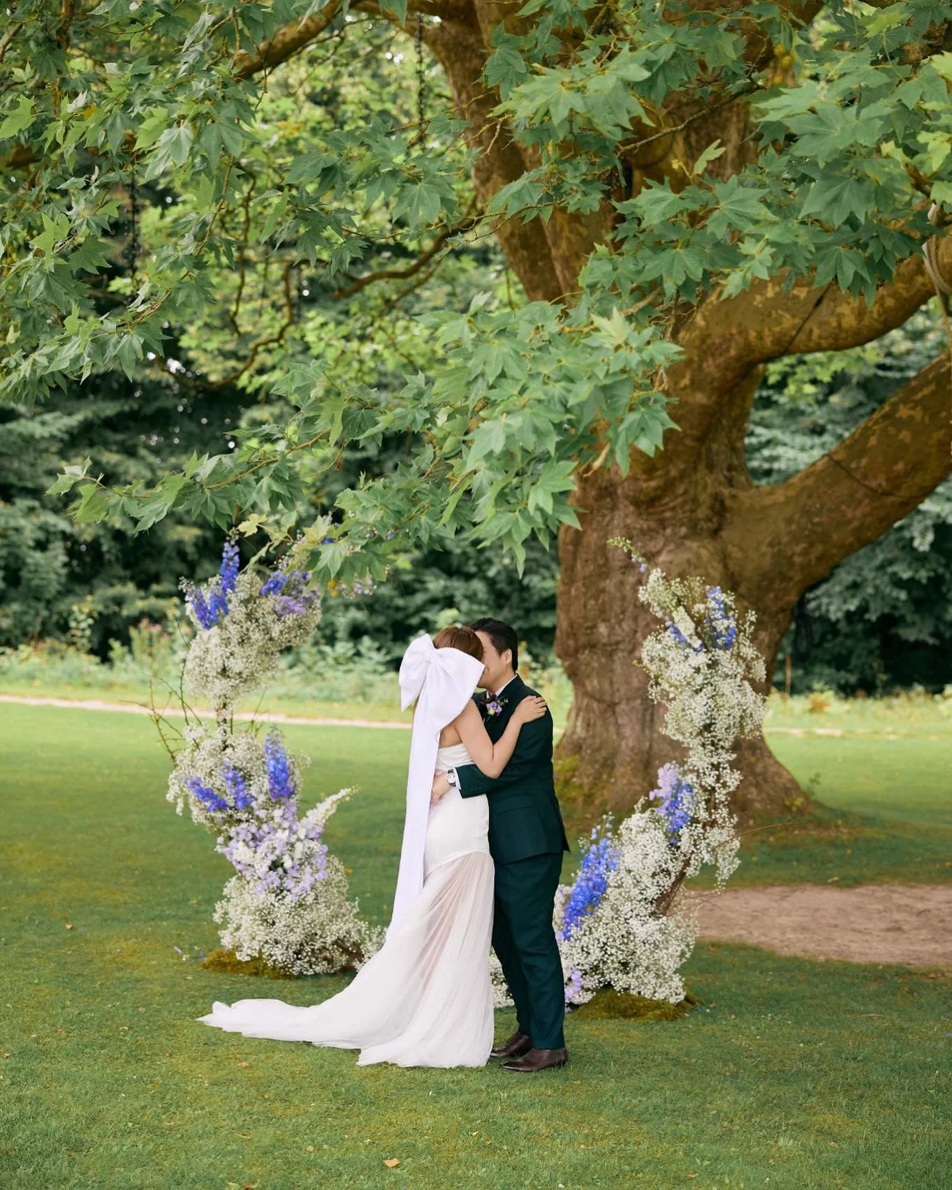 Looking back on this unforgettable summer wedding at @kokkedalslotcopenhagen , where love truly bloomed under the majestic branches of a grand old tree. This floral circle arch, dressed in soft white, blue, and purple delphiniums with delicate baby&r