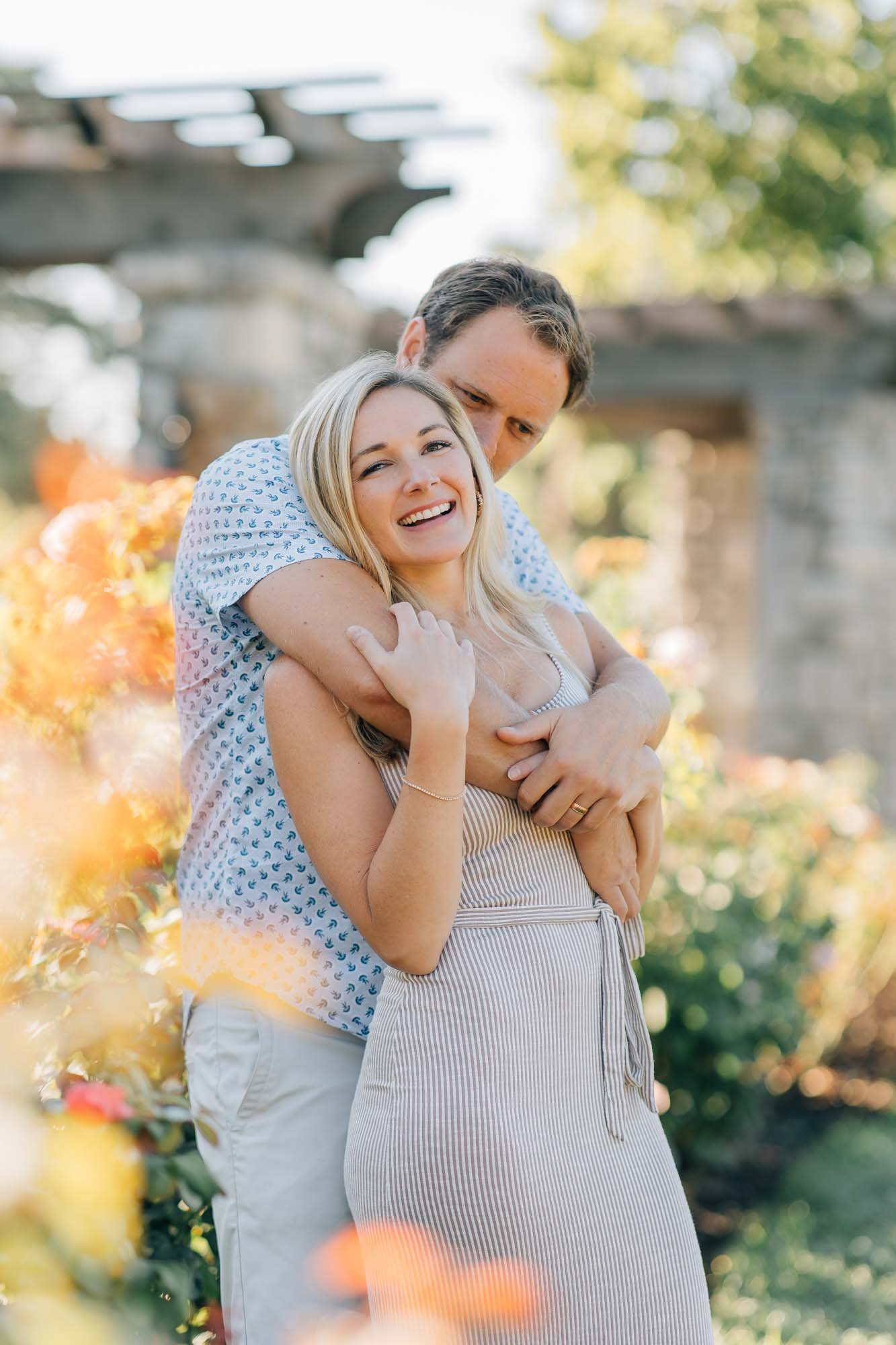 husband hugging wife in a rose garden