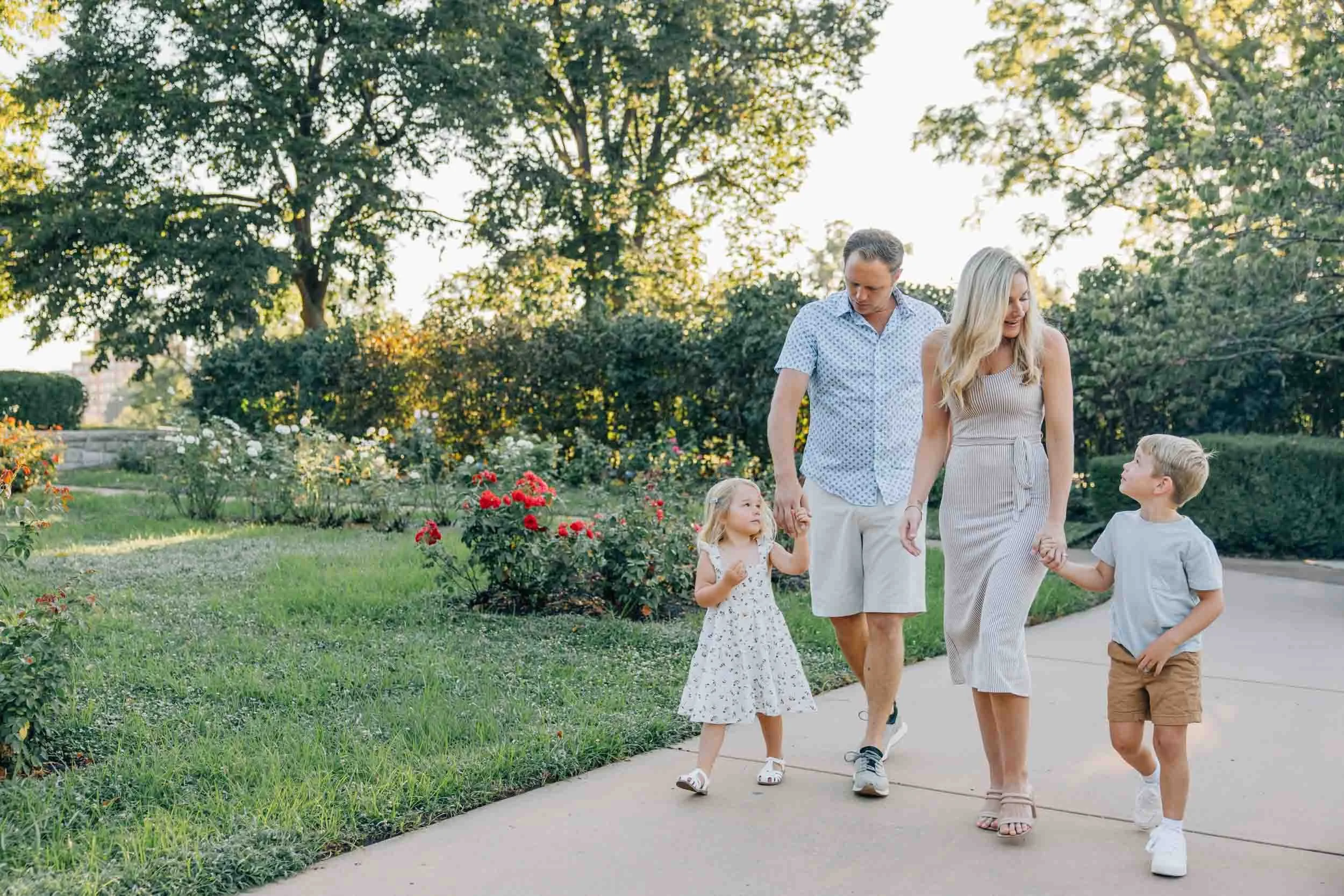 family of 4 walking hand in hand near a rose garden
